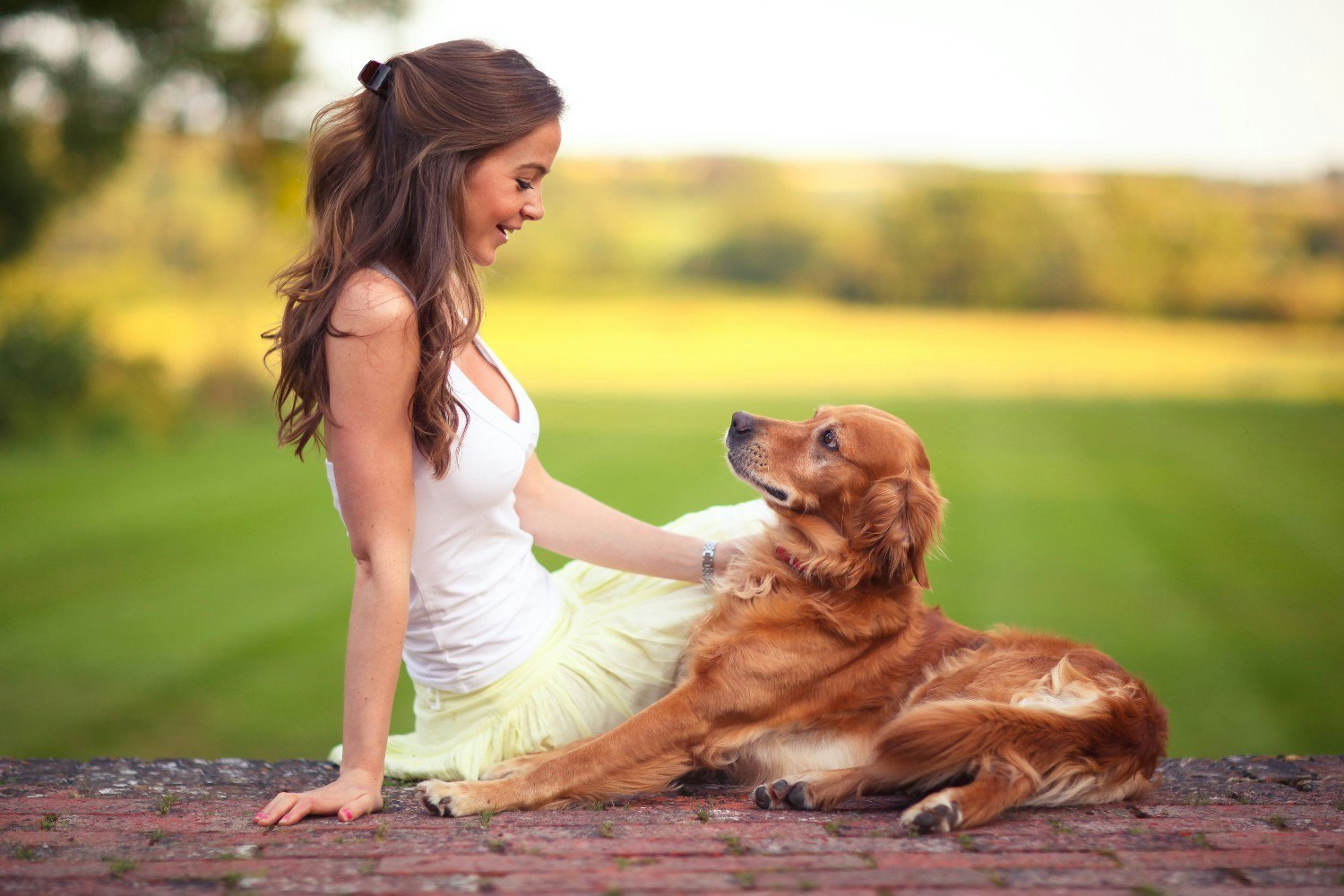 A girl and her dog sitting on the ground with a green field behind them