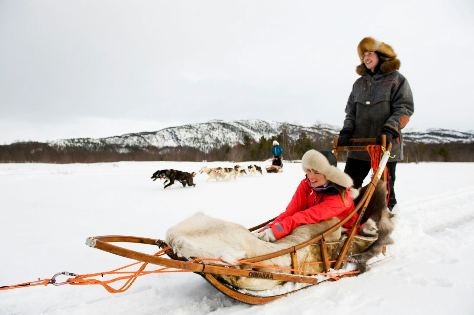 A girl wrapped up warm in a sled being pulled through the snow by huskies