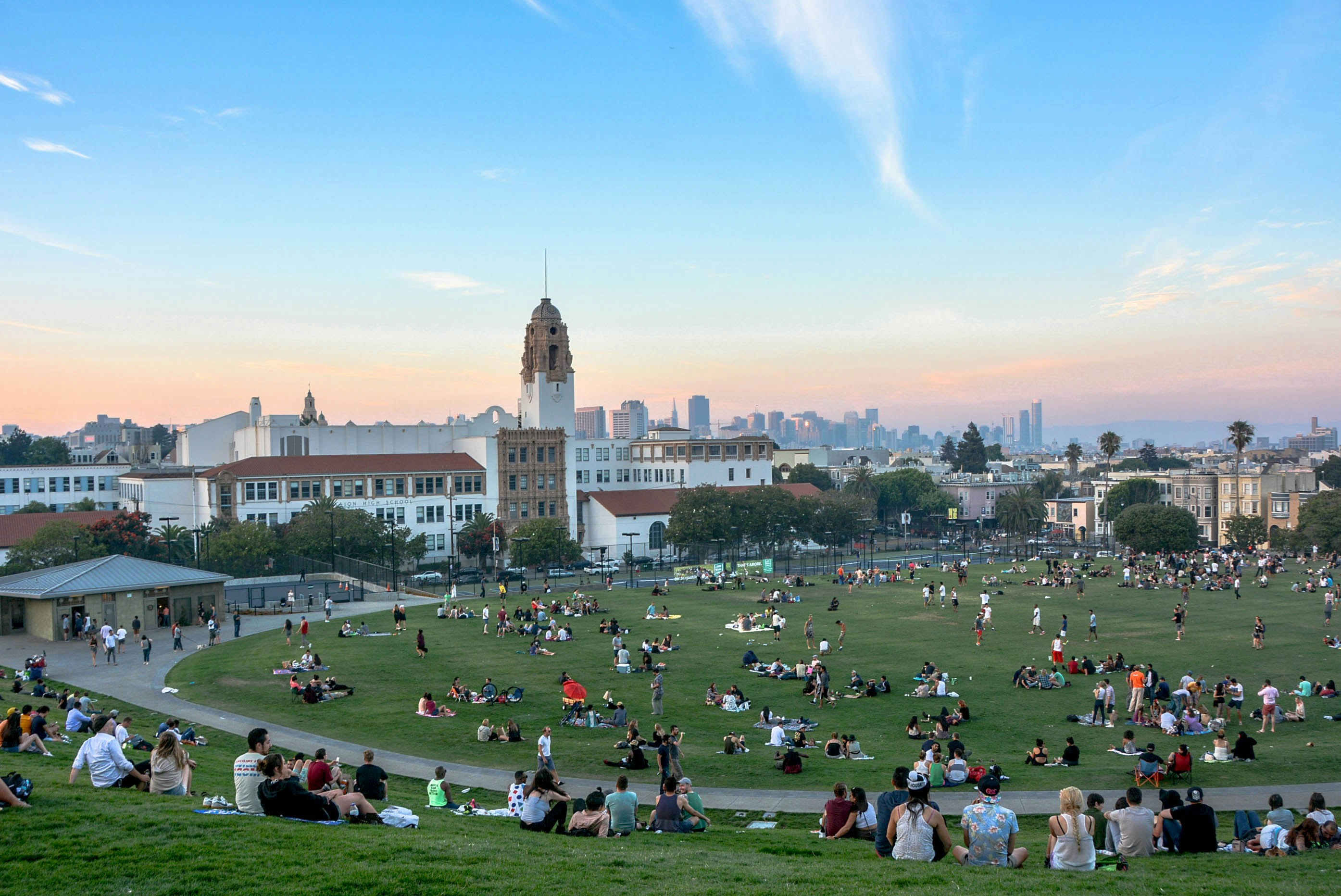 The large green lawn at Dolores Park is filled with people laying on blankets, walking around or playing around.
