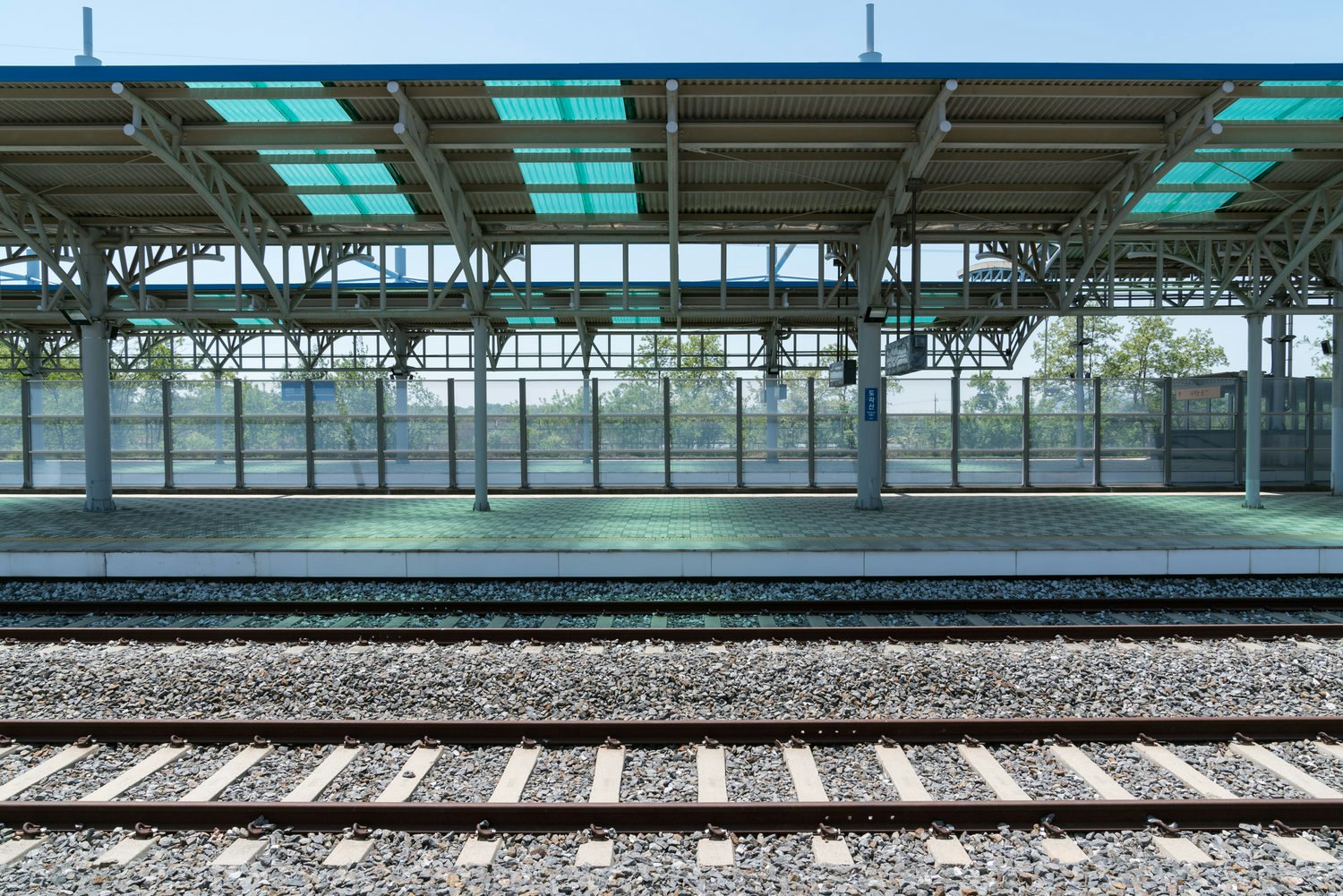 An empty platform at the abandoned Dorasan Station, in Korea. Glass paneling separates the platform from woodland outside, while a track is visible in front.