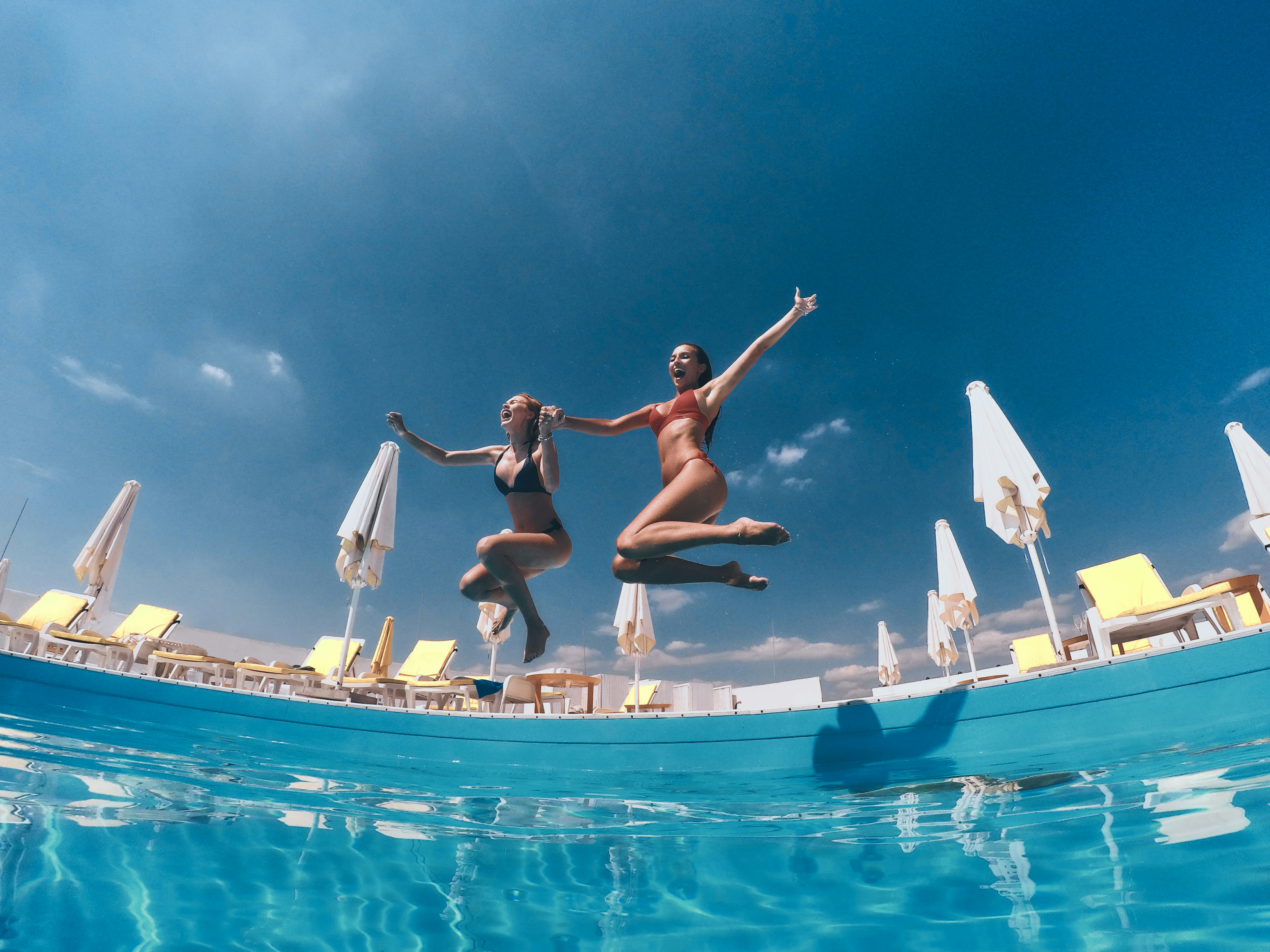 Two friends hold hands while jumping into a pool