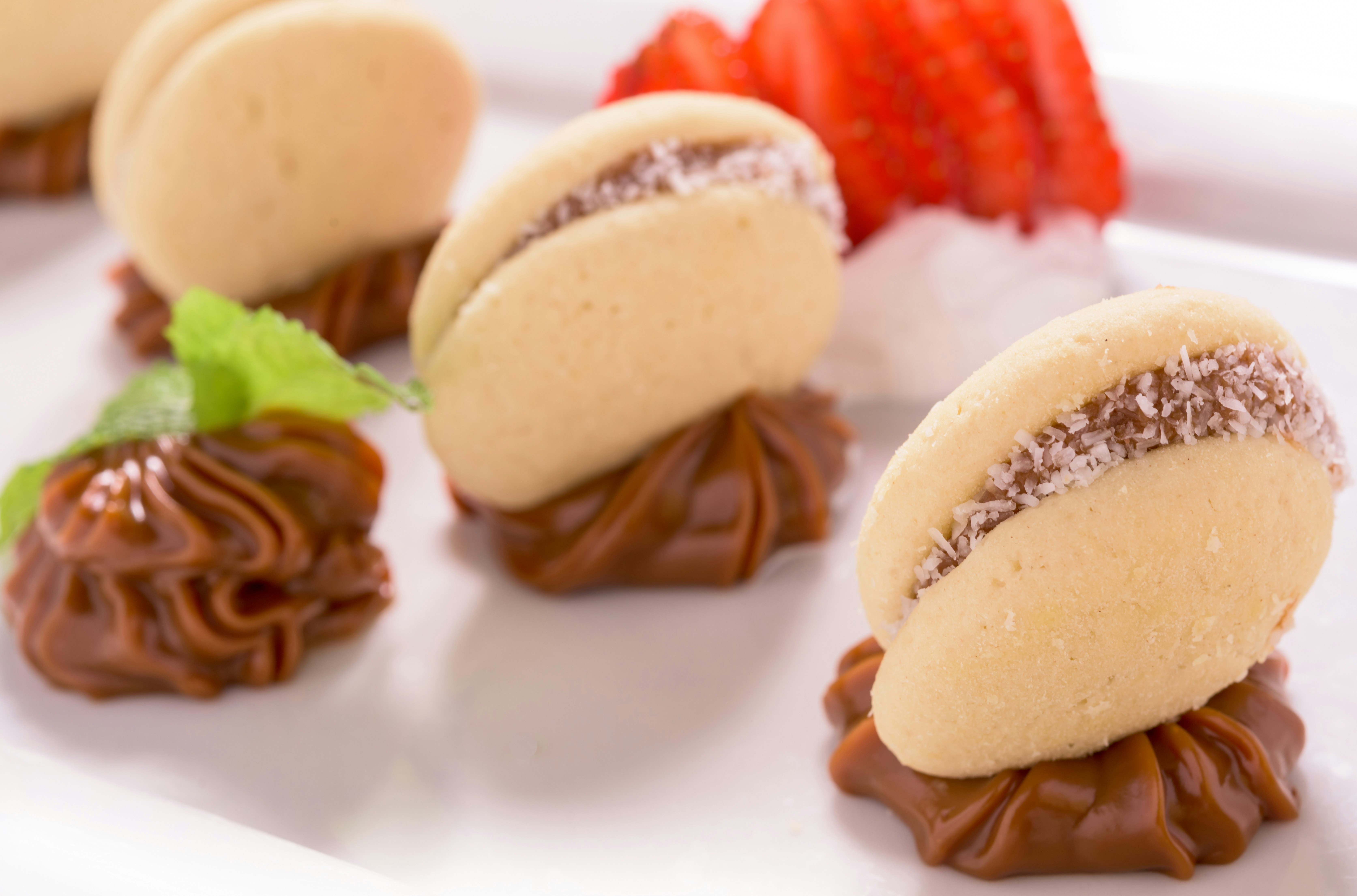 A trio of alfajores rest in a dallop of dulce de leche mousse on a white plate.