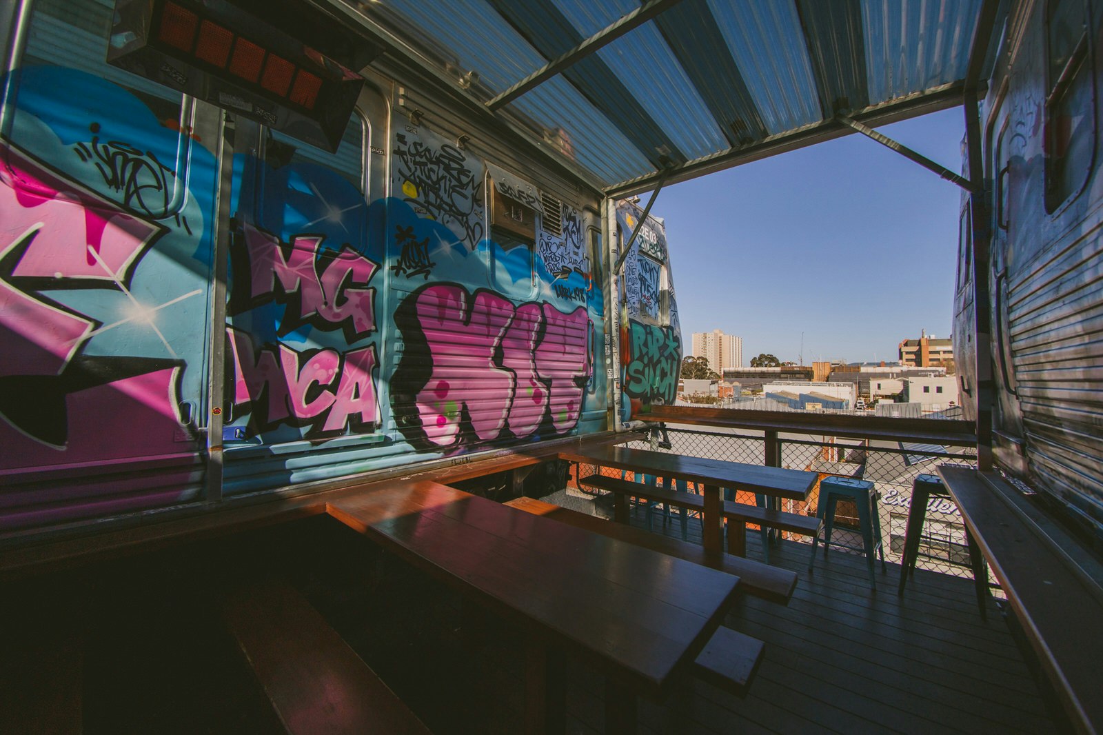 A view of Collingwood, Melbourne from Easey's rooftop bar. Wooden tables and benches are inside old camper vans heavily decorated with colourful graffiti
