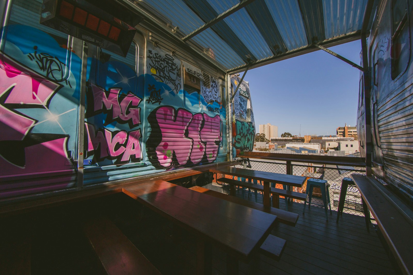 Utsikt över Collingwood, Melbourne från Easeys takbar.  Träbord och bänkar står inuti gamla husbilar som är kraftigt dekorerade med färgglad graffiti