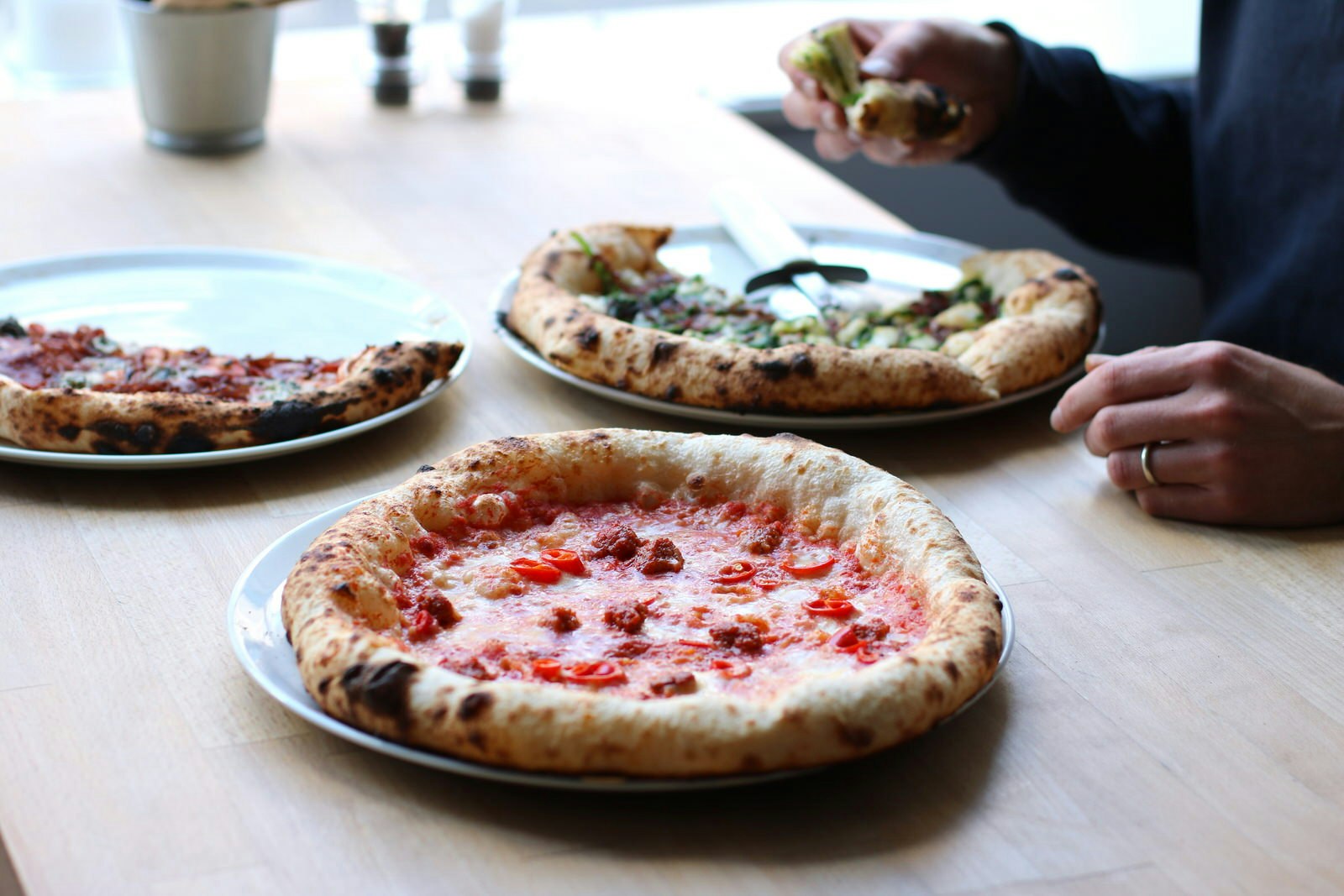 En närbild av tre pizzor på ett träbord, i olika skeden av att ätas i East Pizzas, Edinburgh.