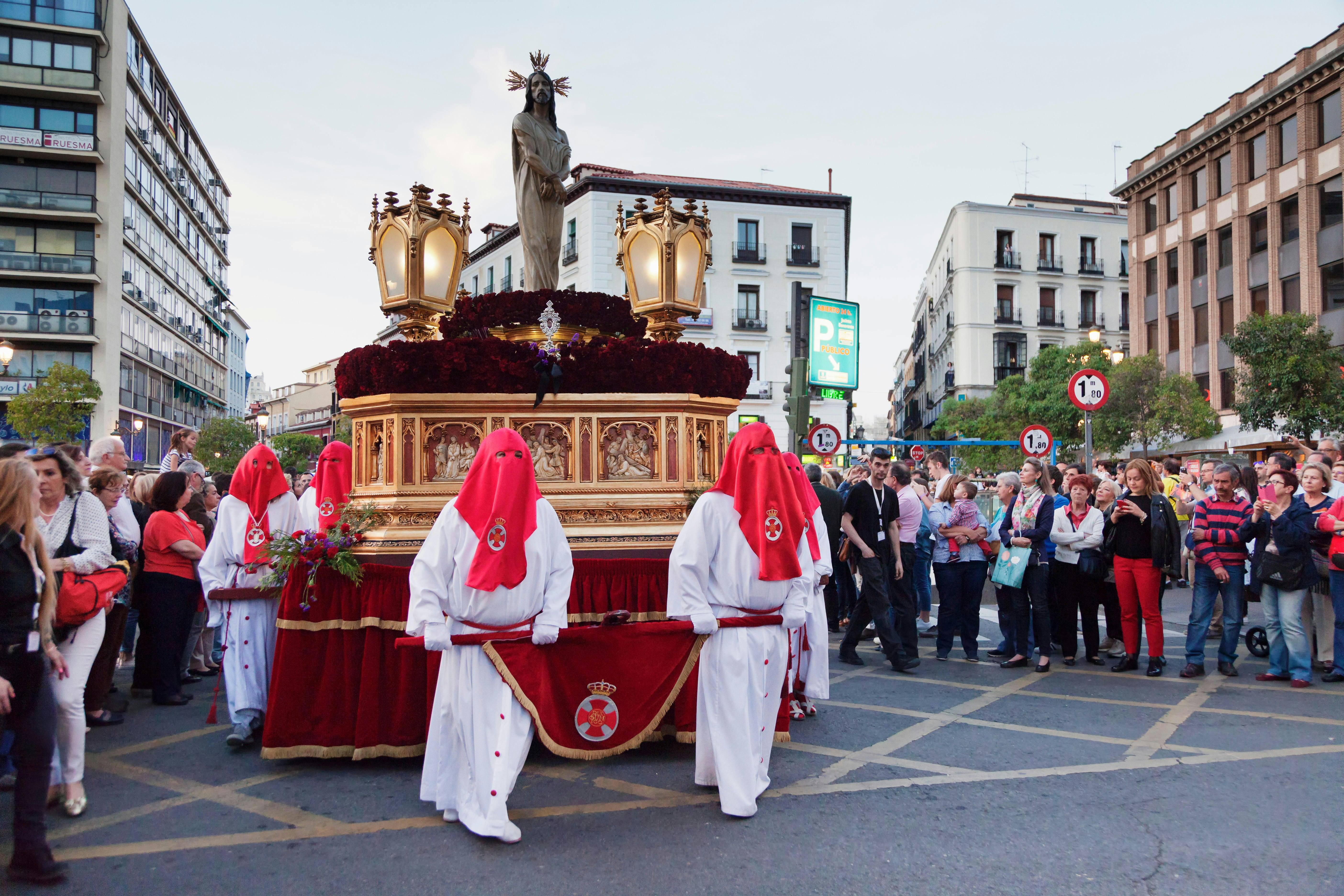People parading through the streets dressed in white robes with red hoods covering their faces during Semana Santa in Madrid, Spain.