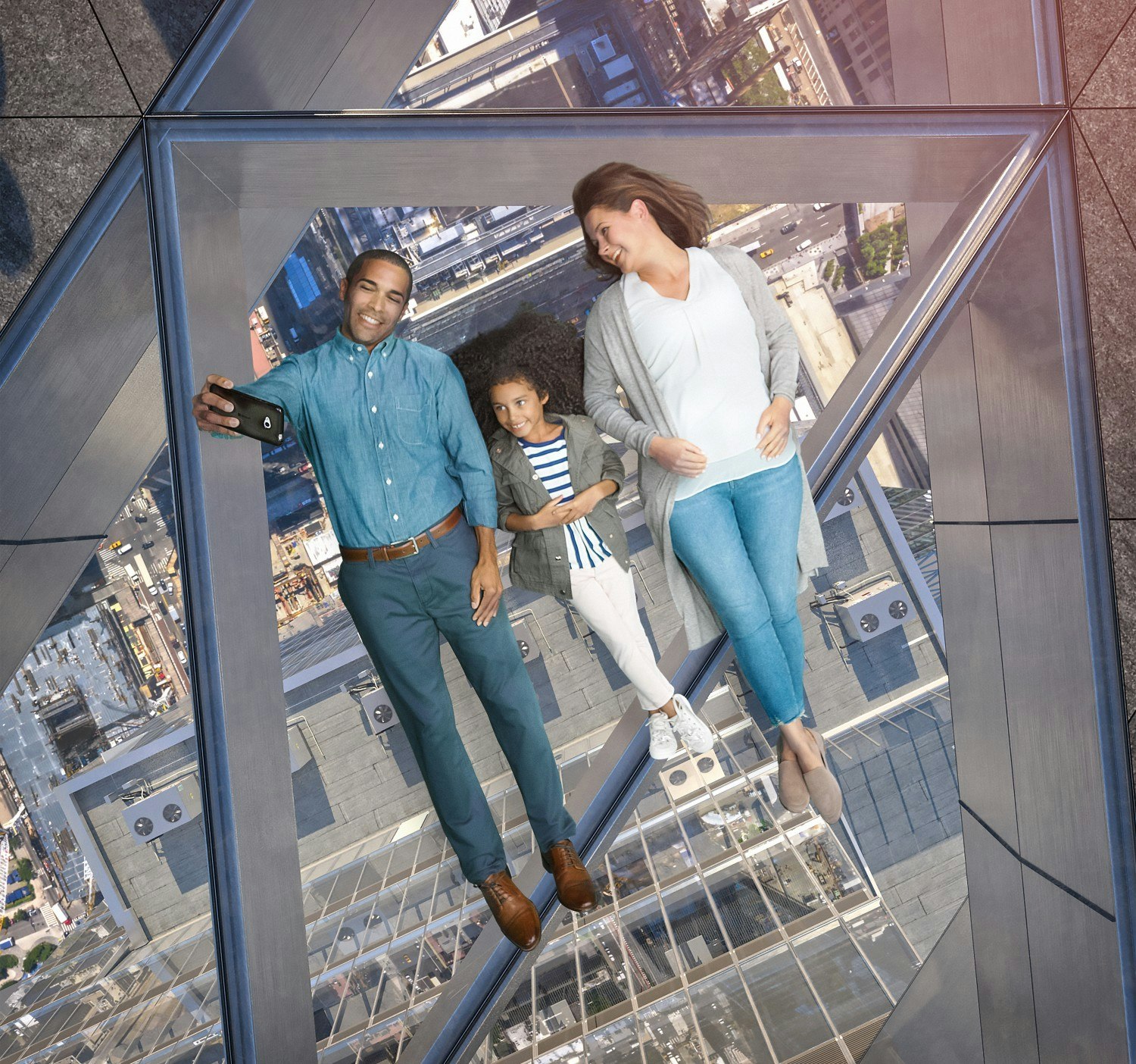 Three people lying on a glass observation deck in New York