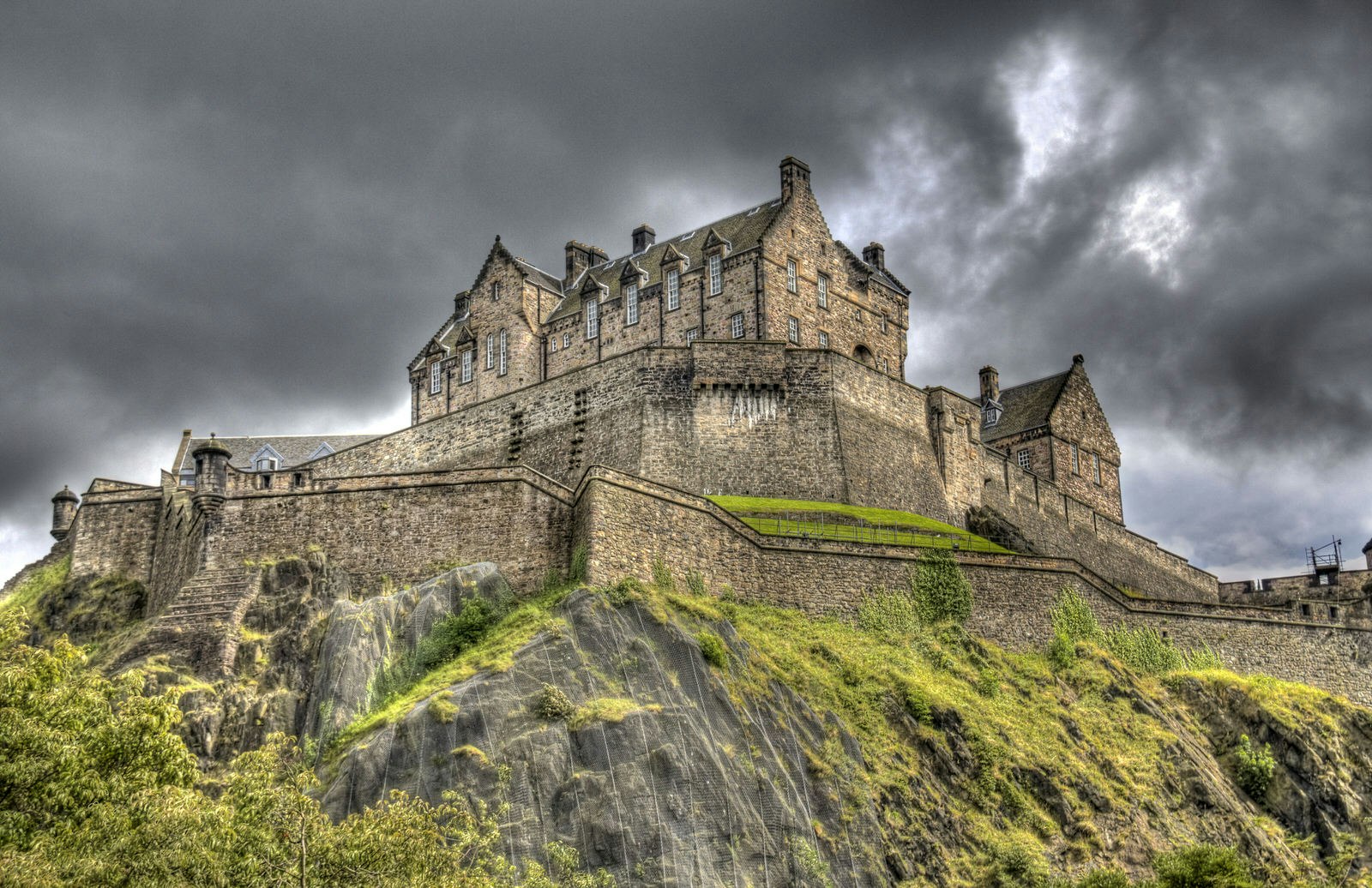 Low-angle view of Edinburgh Castle on Castle Rock with dark clouds.