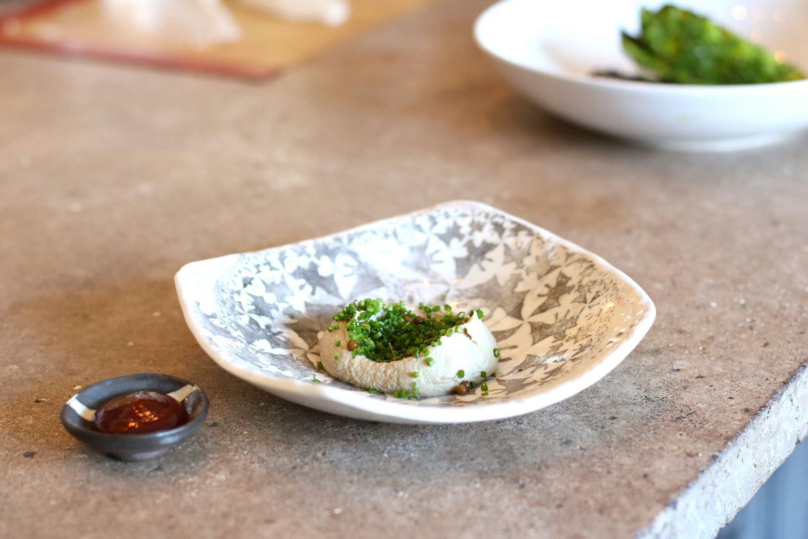 A close up of a truckle of goats cheese, covered in herbs and served in a hand-crafted dish.