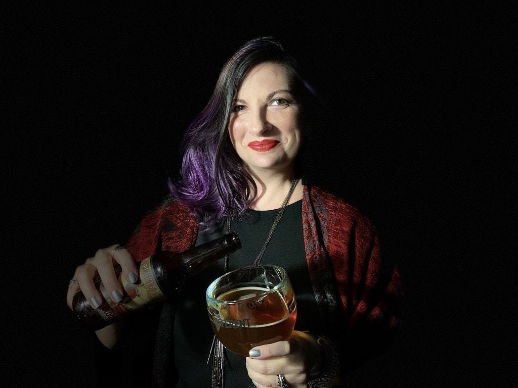 A woman with black and purple hair pours a beer into a glass