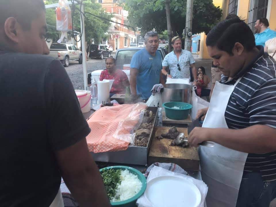 A man chops up meat on a wooden cutting board at a street food stall in Puerto Vallarta. There is a crowd of customers waiting to get served. 