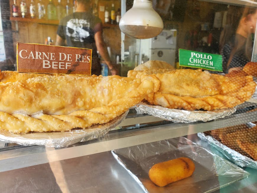Two plates, one containing beef and chicken empanadas sit behind a glass window at kioskos in Puerto Rico 