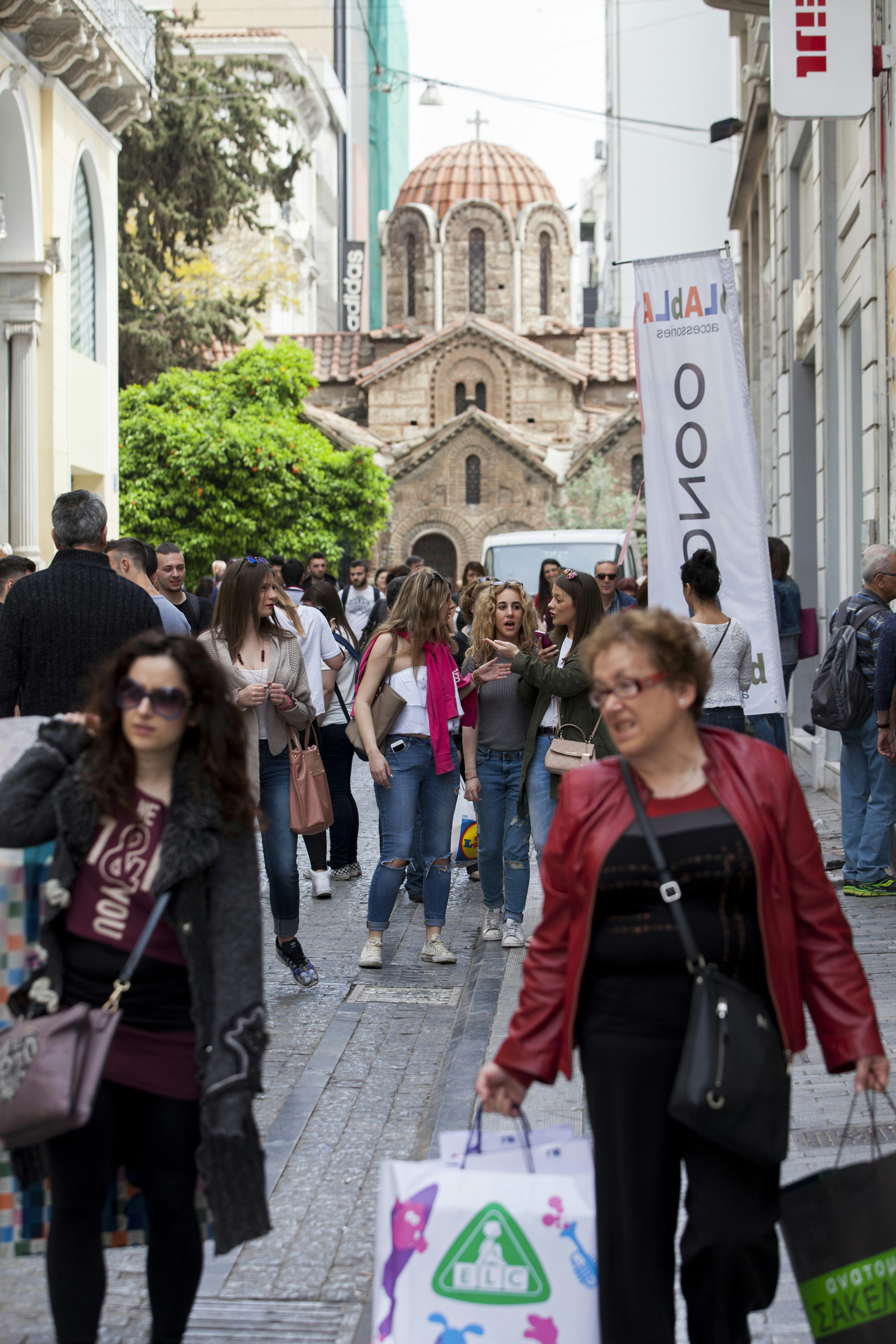 A woman with shopping bags walks down shop-lined Ermou St in Athens, Greece