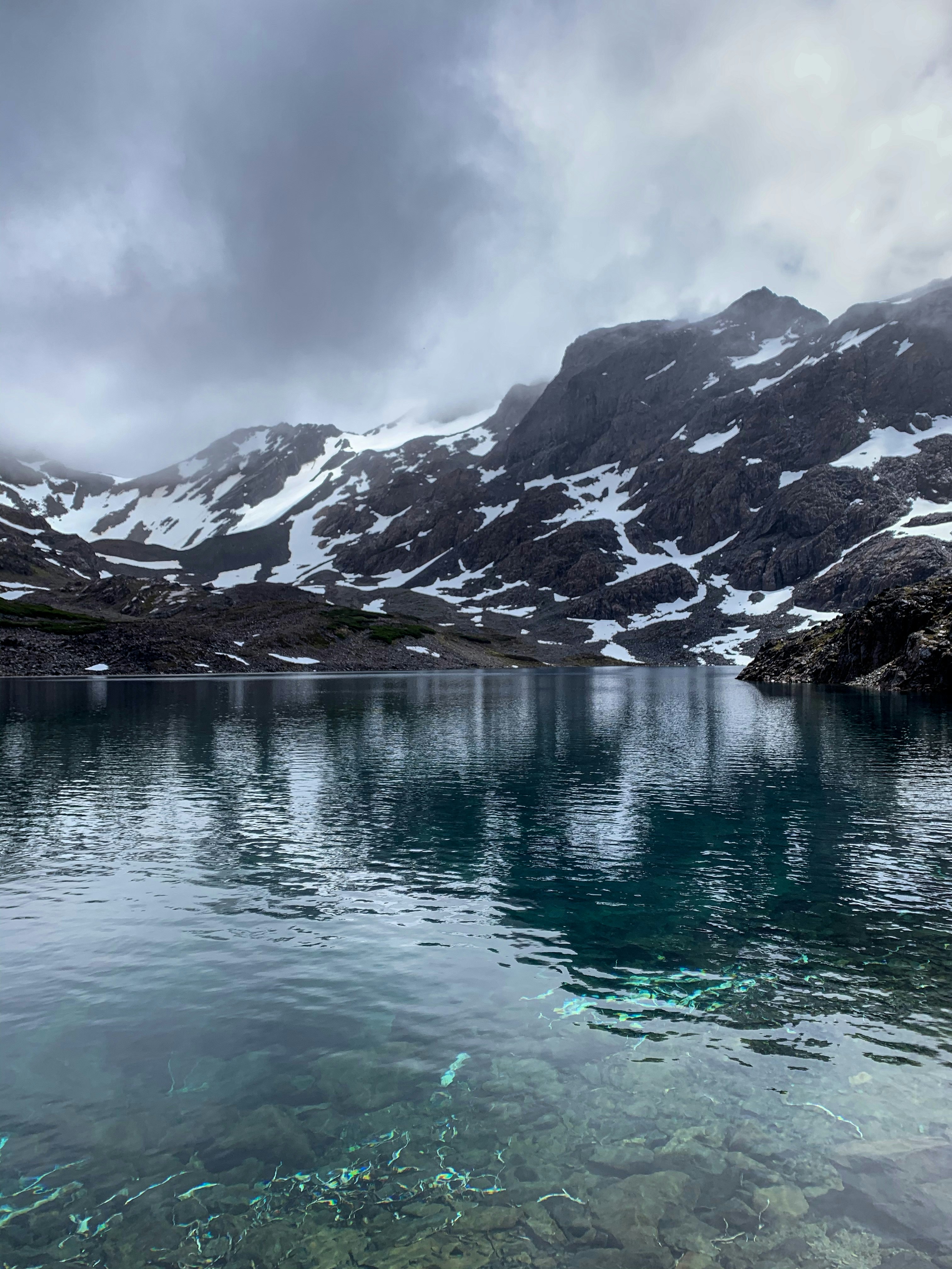 A shoreline shot of glassy Laguna Escondida, surrounded by high, snow-laden mountain slopes.