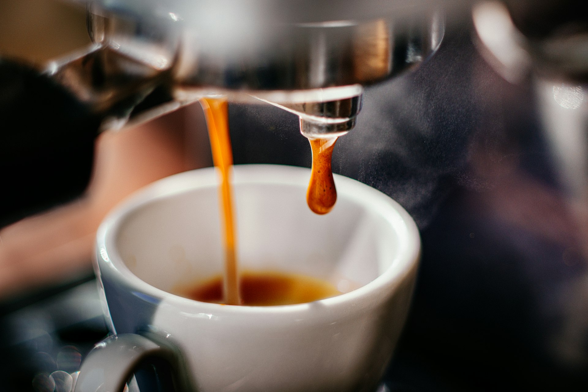 Closeup of a machine pouring espresso into a small white cup