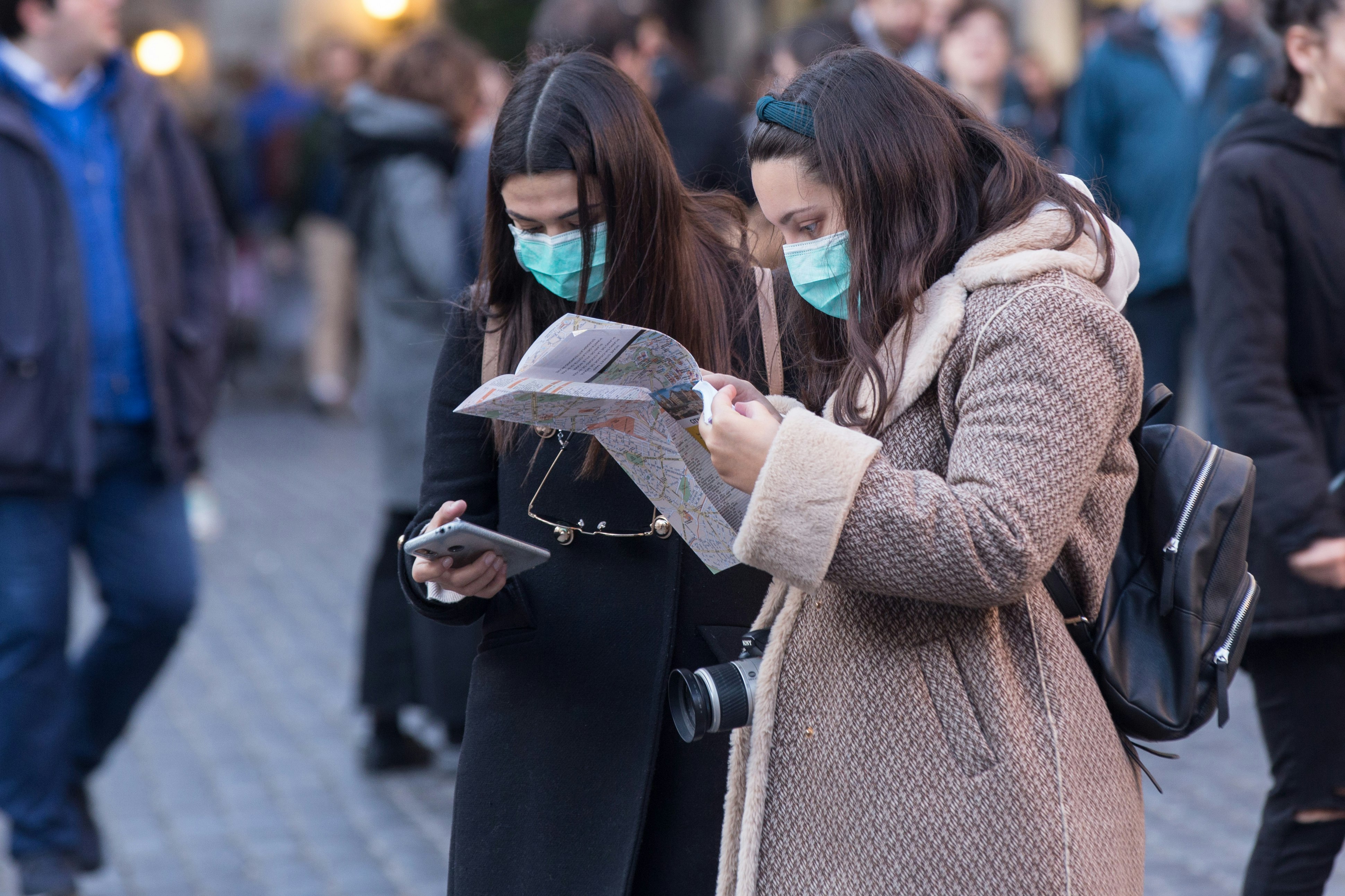 Two young women wearing face masks in Rome look at a map