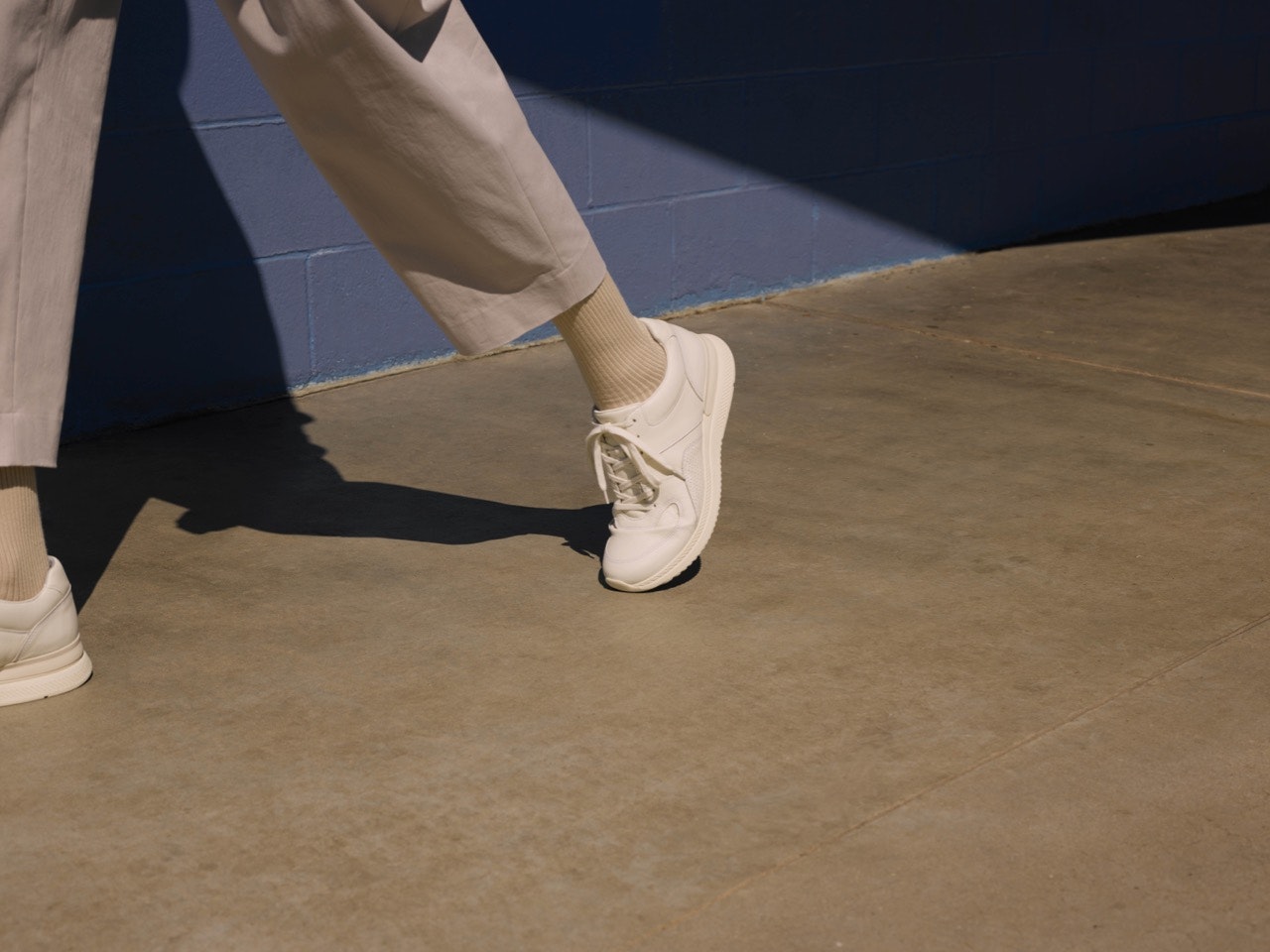 Closeup of a lower leg in khaki pants, foot wearing Everlane's Tread trainer in white