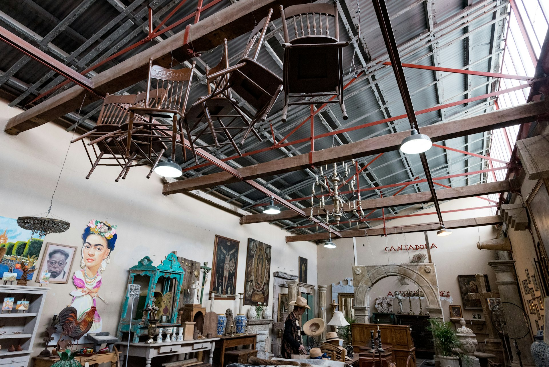 Chairs dangle from the wooden ceiling beams of a design complex, Fábrica La Aurora, where at ground level ornaments, homewares and antiques are on display