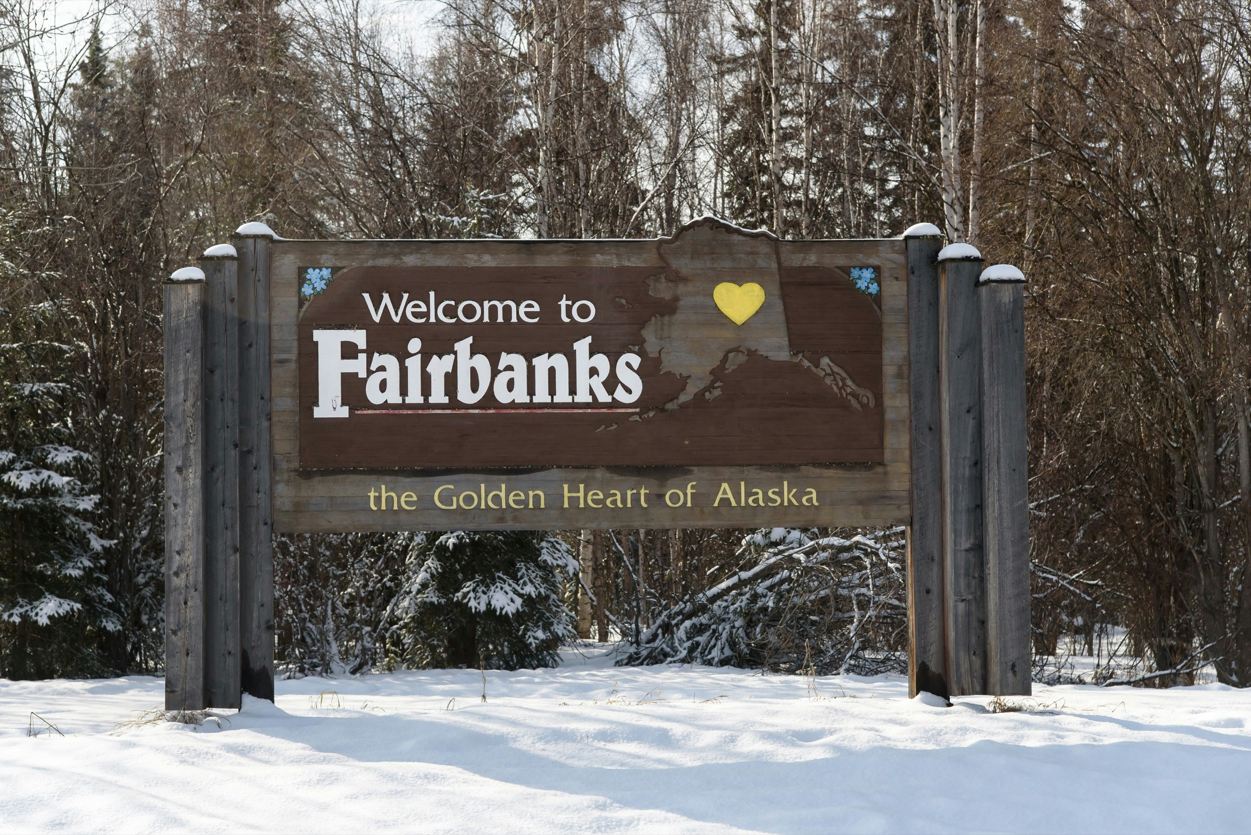 A wooden sign says welcome to Fairbanks, with a golden heart shape in the middle of an image of the state