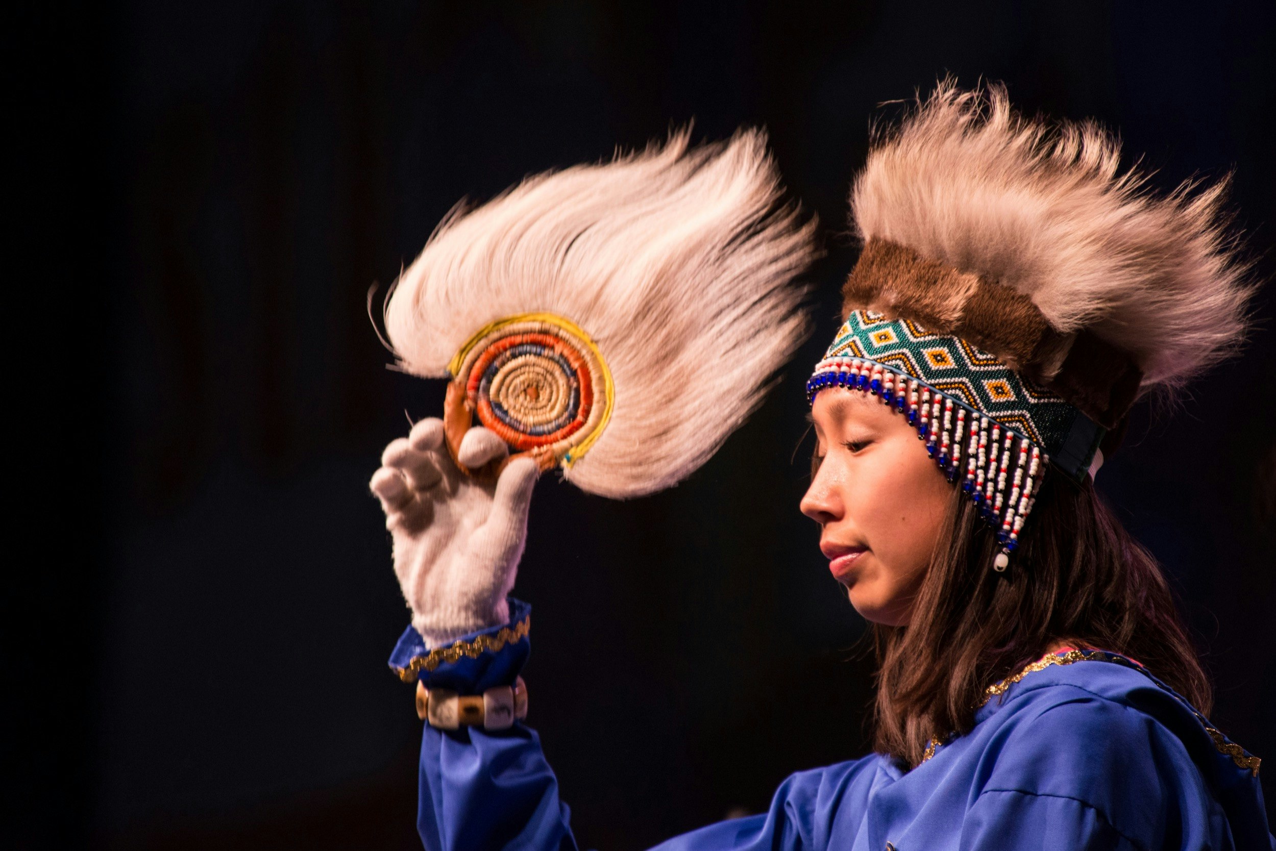 An Alaska Native does a traditional dance on a black background