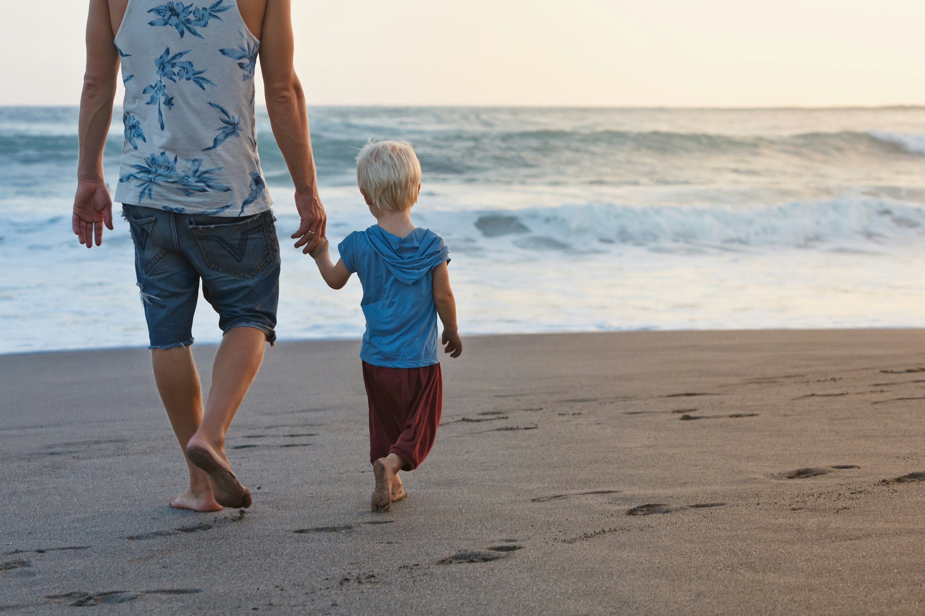 A father and son are holding hands as they walk down the beach