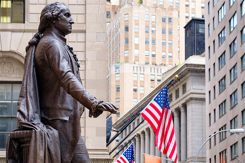 Federal Hall - free things NYC.jpg A statue of George Washington at the Federal Hall in New York City. American flags hang around the statue, along with towering skyscrapers.