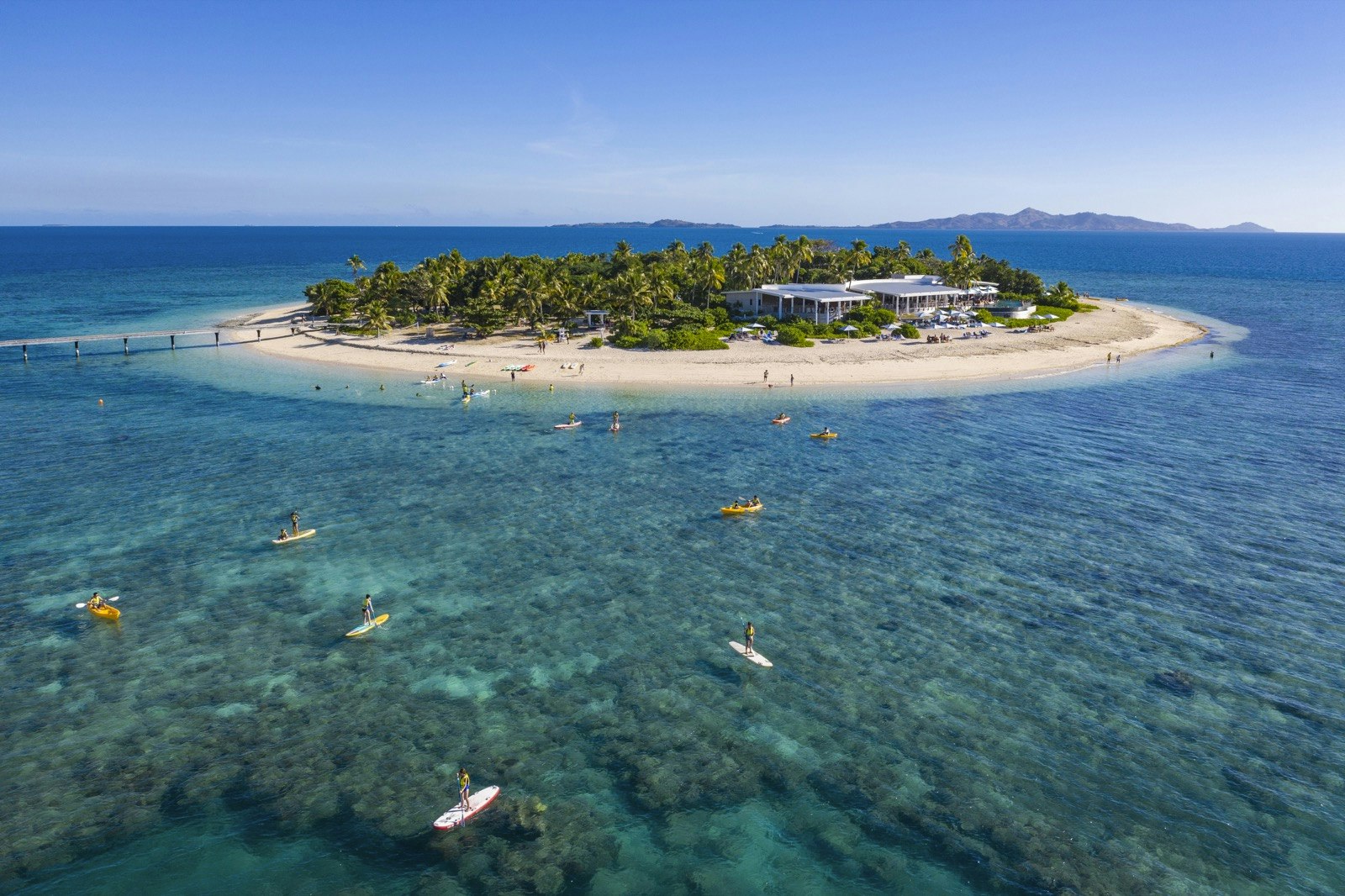 An aerial photo of a resort on an island with people practicing water sports