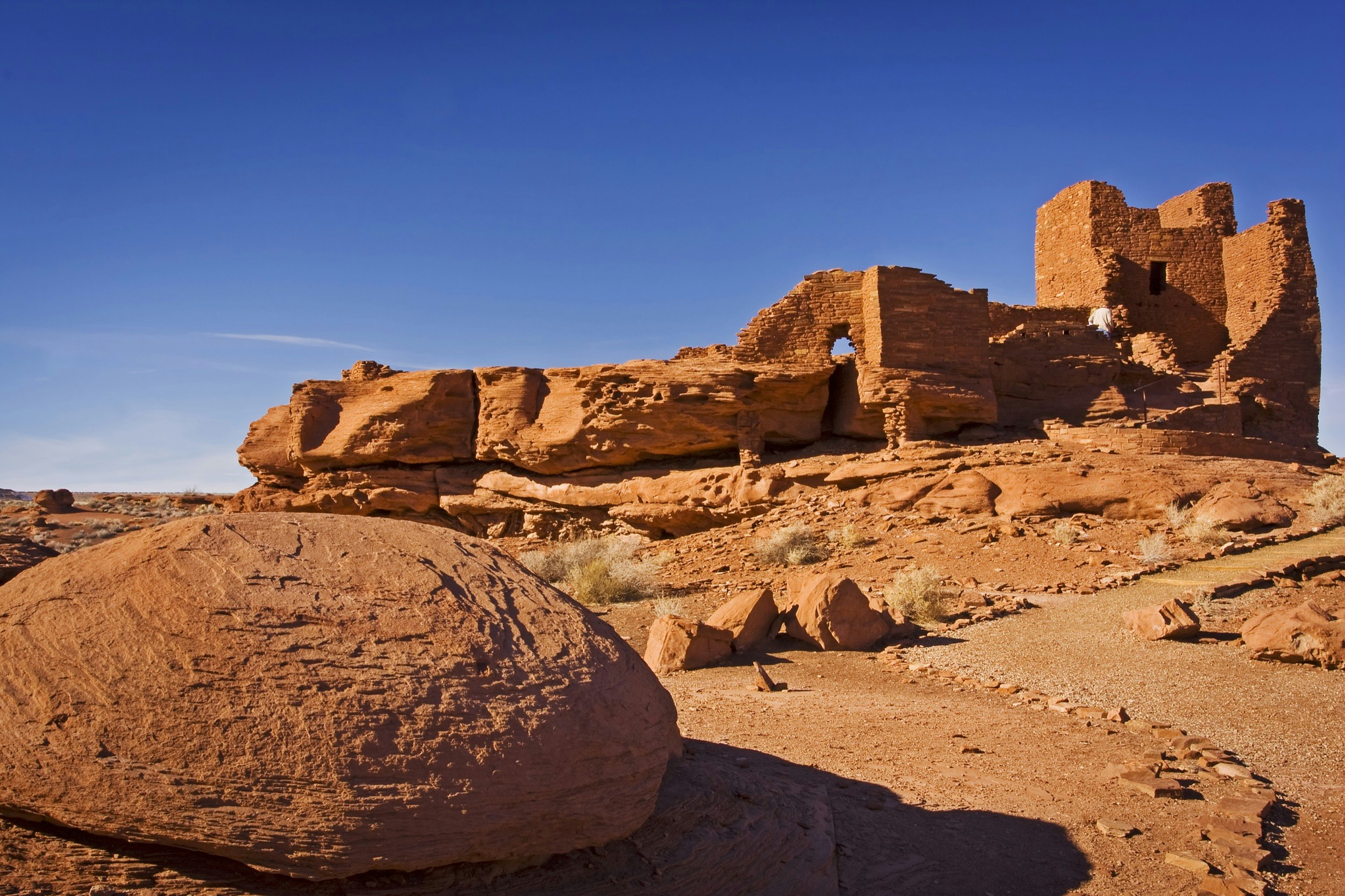 Tourists explore the red orange Wukoki Pueblo Ruins of Wupatki National Monument.