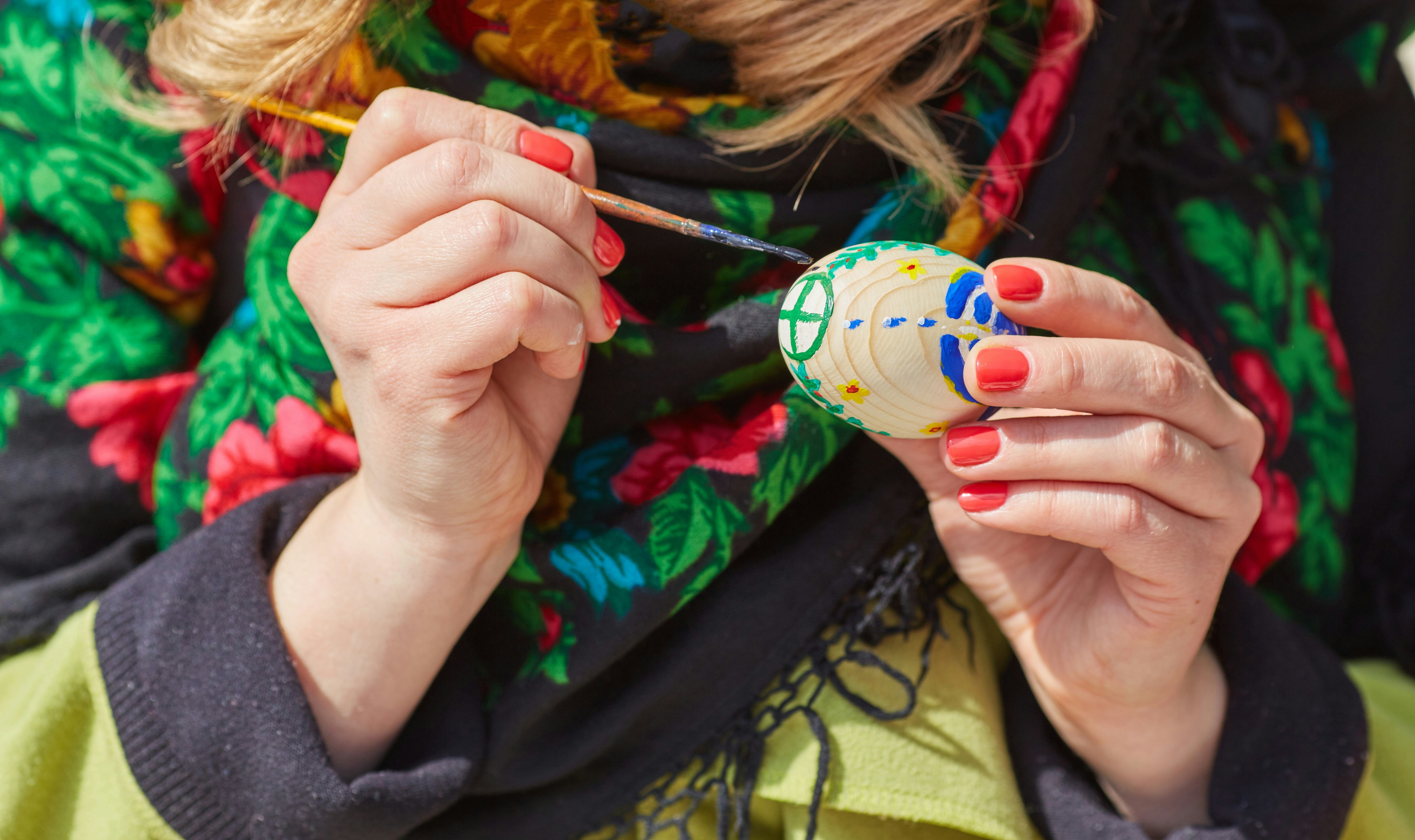 A woman using a fine paintbrush to paint the shell of a hard-boiled egg with an intricate, traditional folk design.