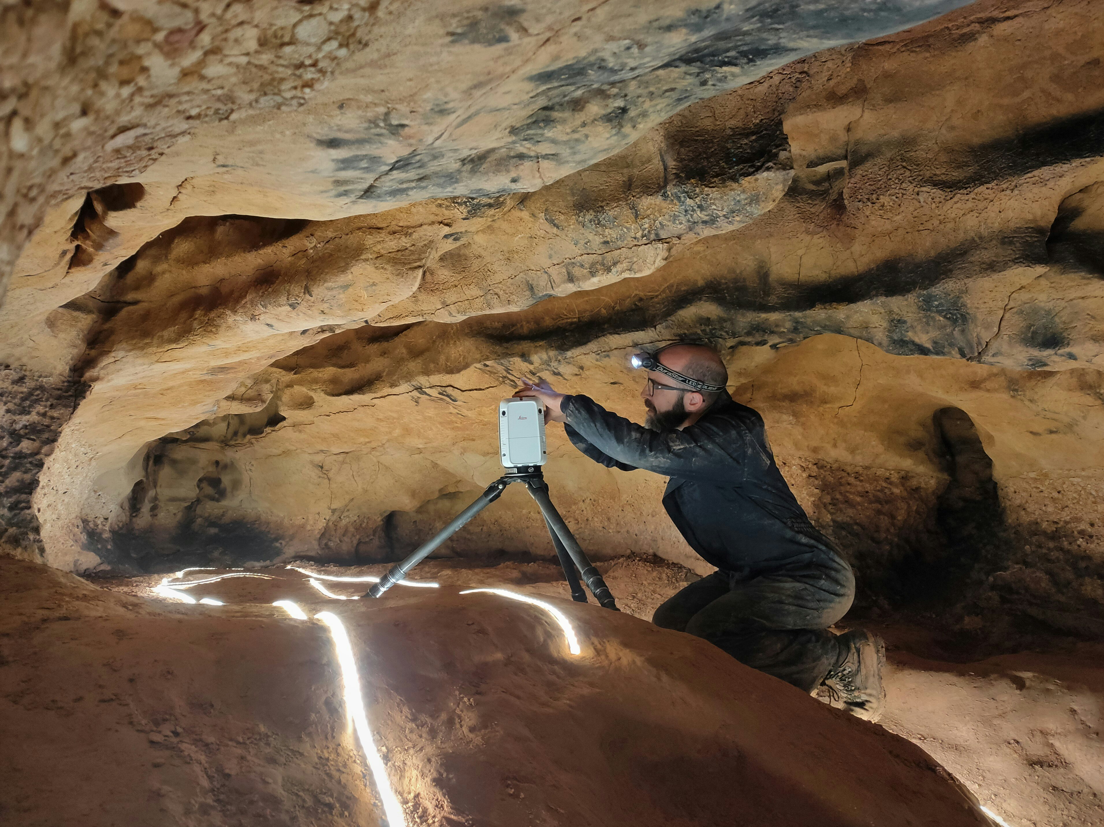 An archaeologist wearing a hard hat examines ancient cave art