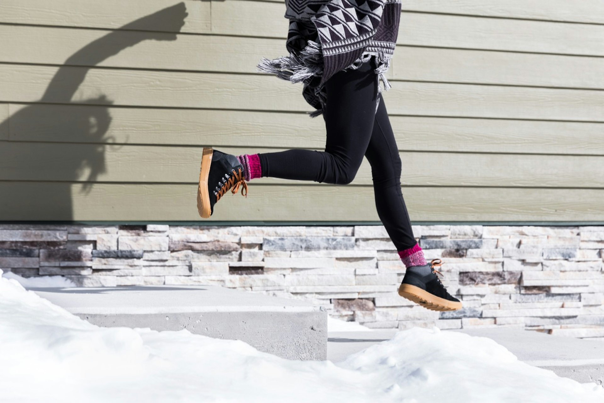 a woman jumping down snow-covered steps wearing Forsake's Lucie Mid boot in black