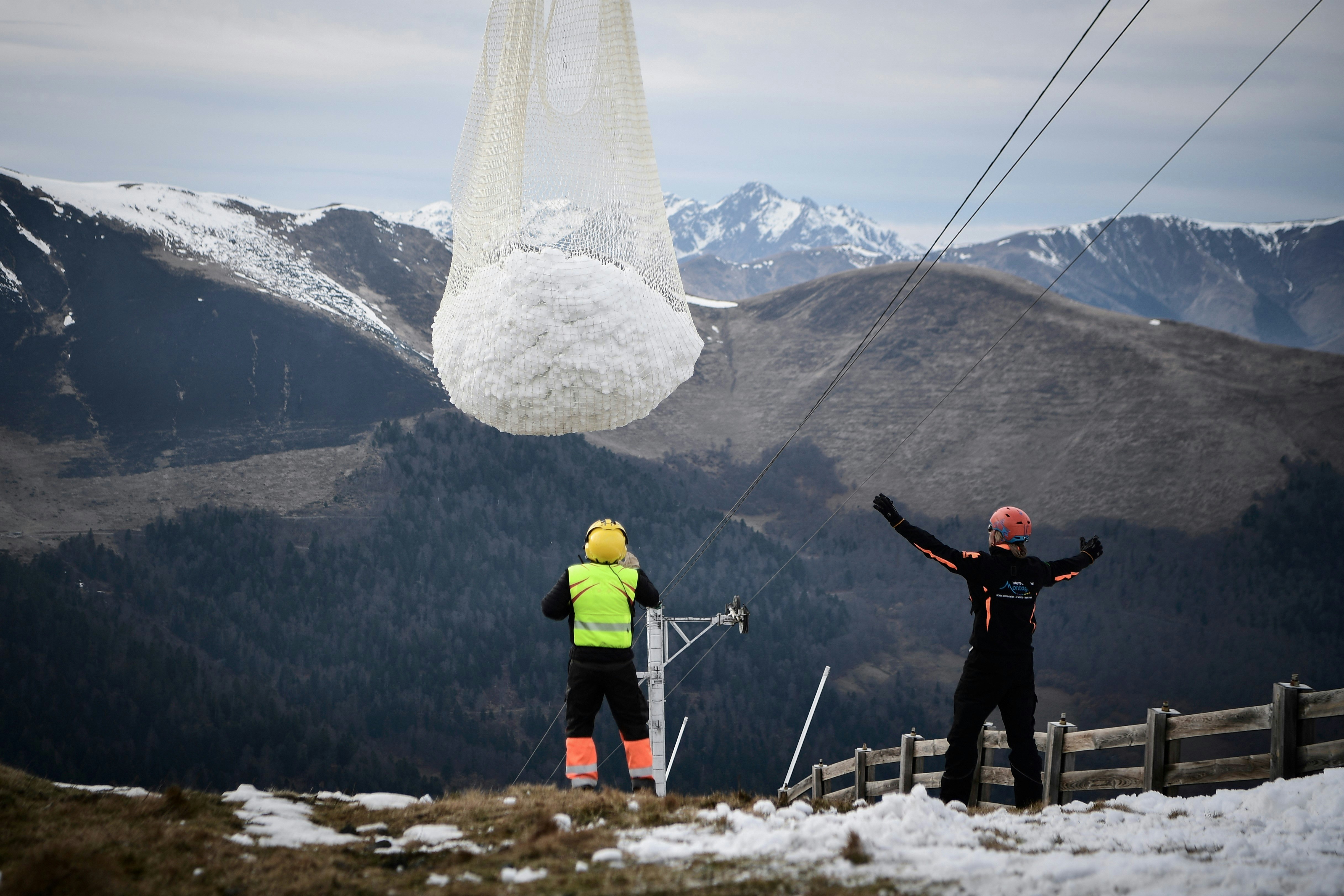 People look at an helicopter carrying snow in order to place it on a ski slope in the Superbagneres station