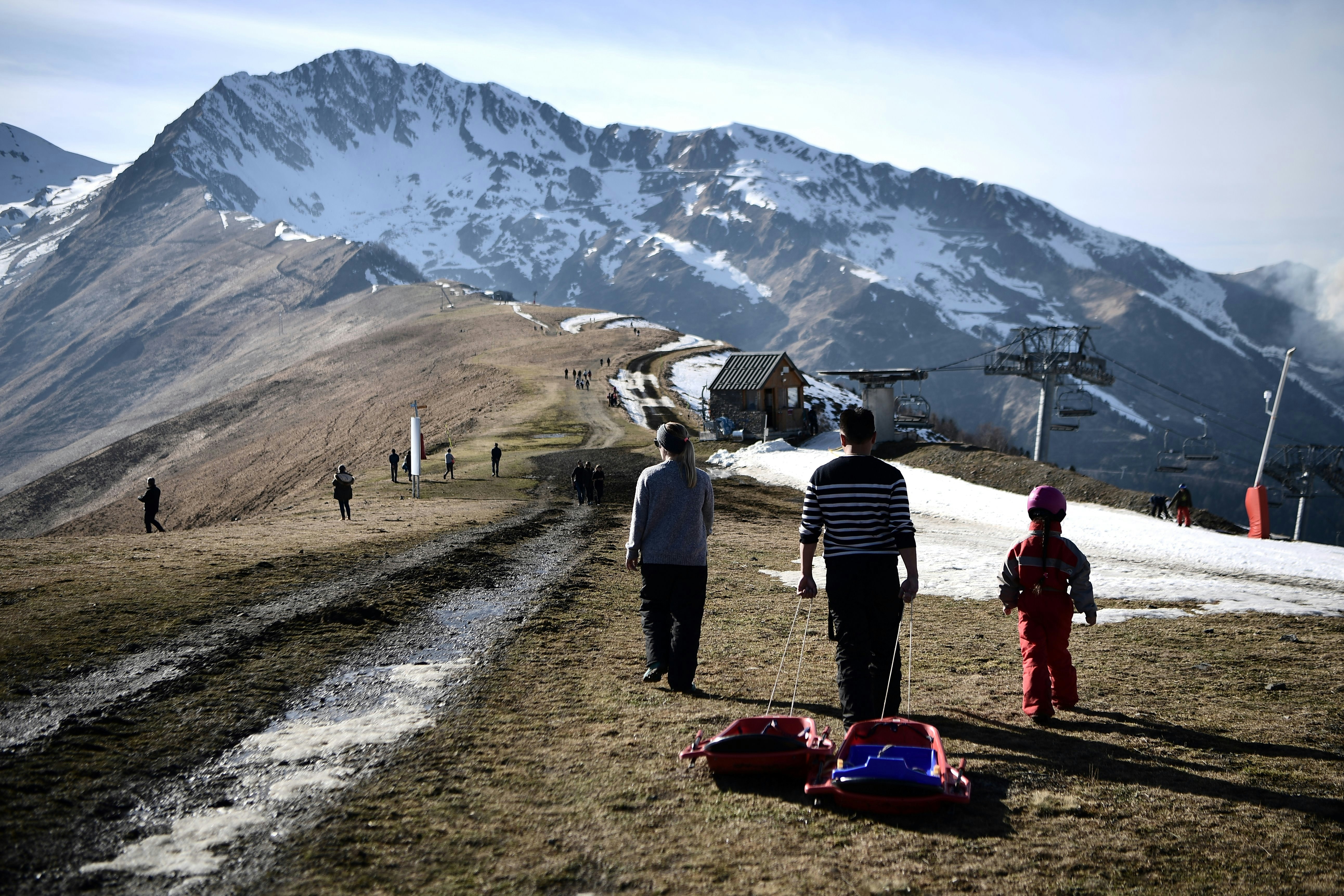 People pull a sled on the top of a bare ski slope 