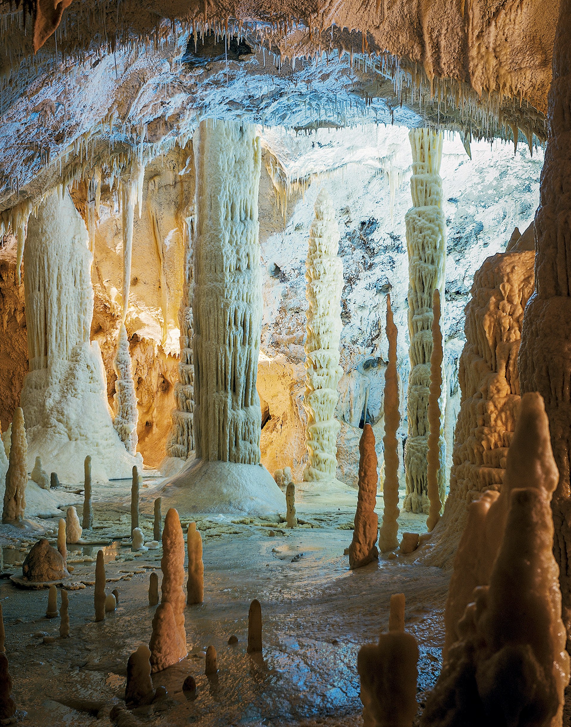 Large stone columns stretch from the floor to the ceiling of a white cavern. Grotte di Frasassi. Le Marche, Italy.