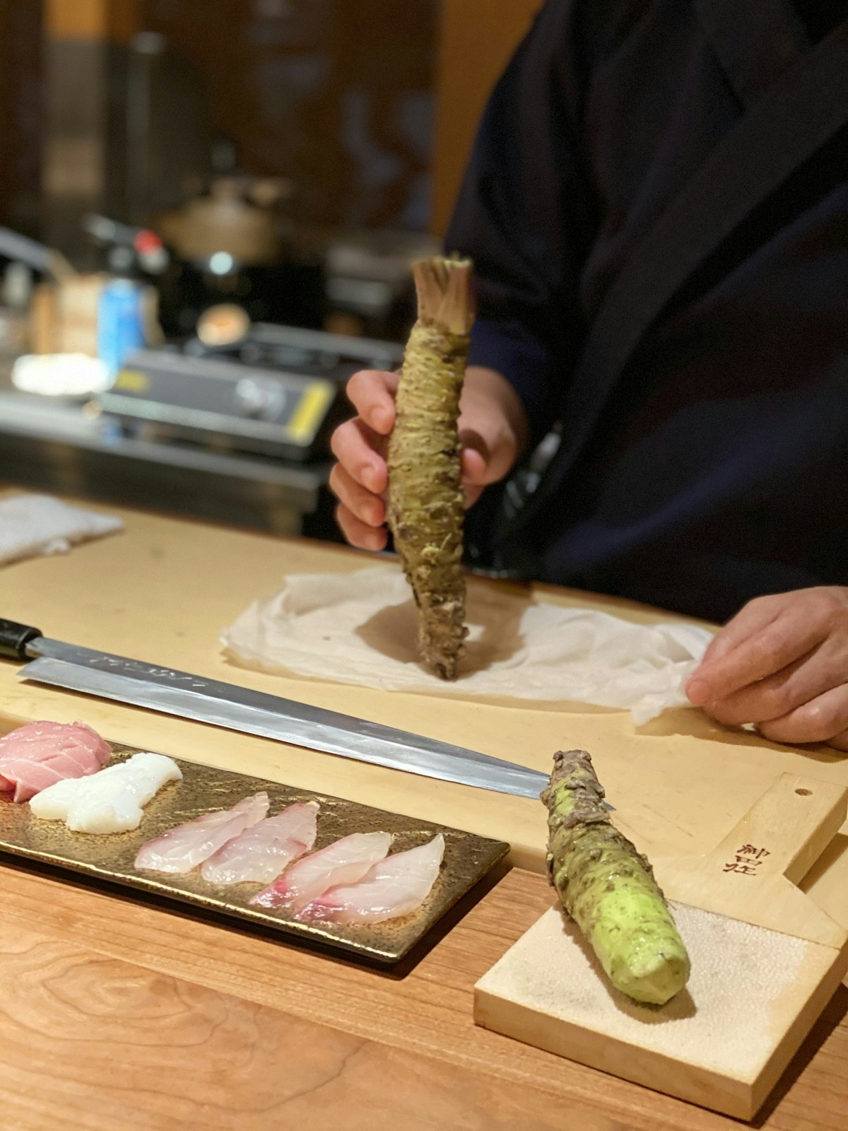 Fresh wasabi being prepared at Sake no Hana by a chef in a navy uniform. The green root is being grated on a wooden board covered with shark skin.