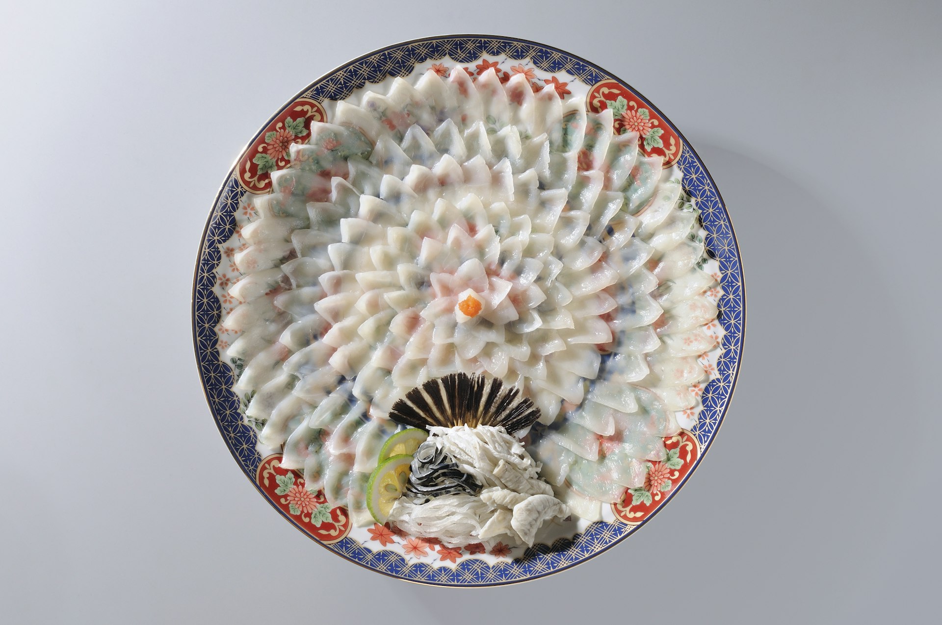 Tunt skivad fugu (pufferfisk) är intrikat arrangerad i form av en blomma på en färgglad tallrik. 