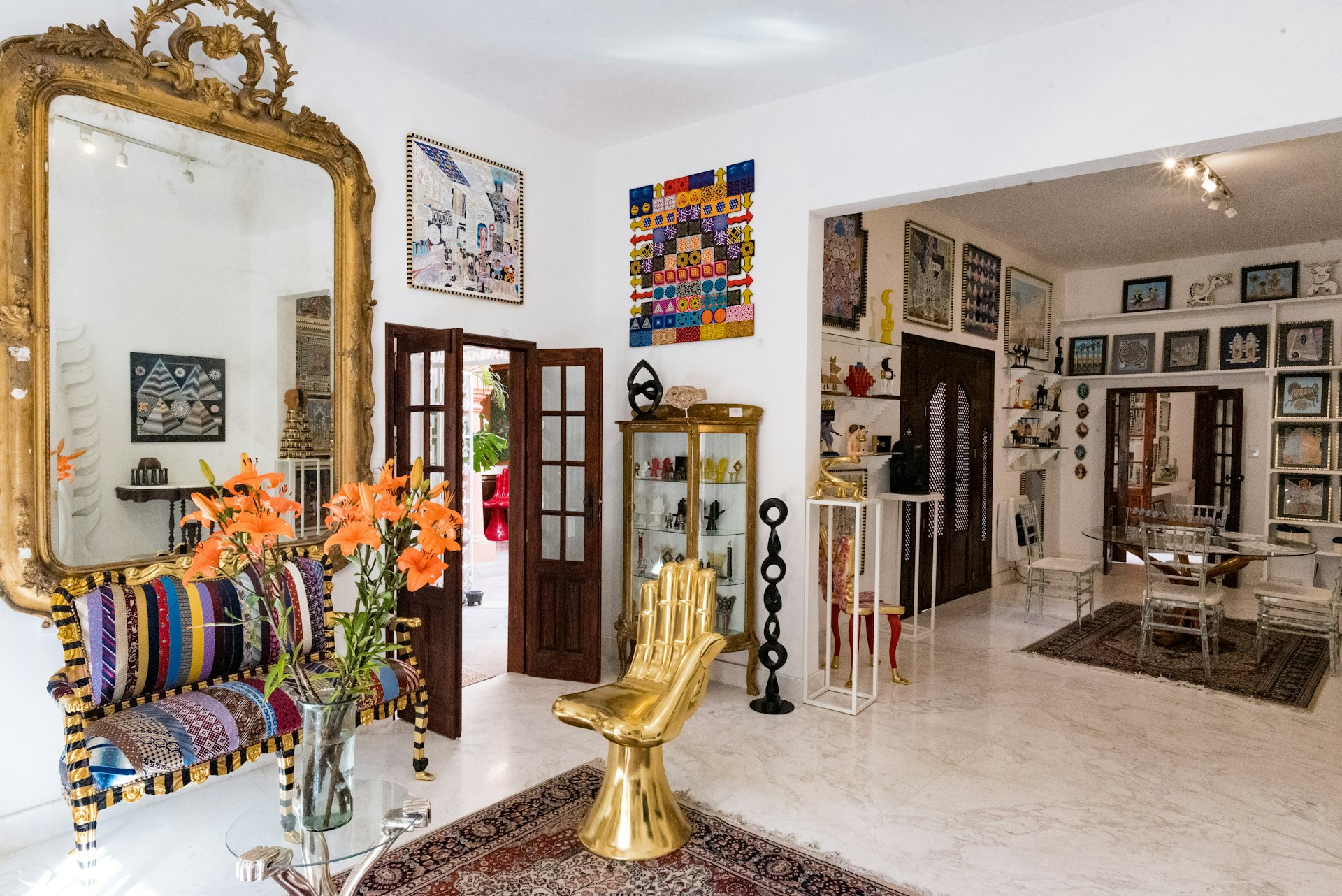 A large brass-frame mirror and a golden chair in the shape of an up-turned hands are the focal points of a large, white-walled design shop. Tasteful rugs, wall hangings and pieces of art are scattered throughout