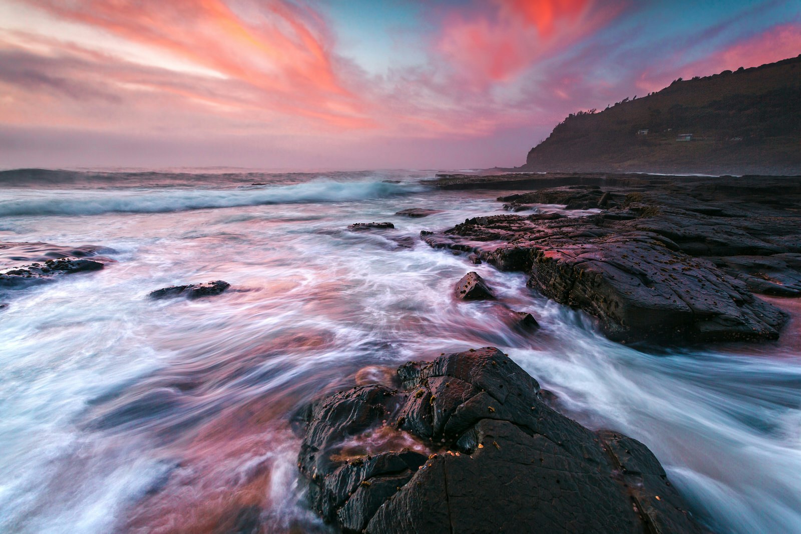 Waves wash onto coastal rocks with colourful clouds in the sky, Garie Beach.