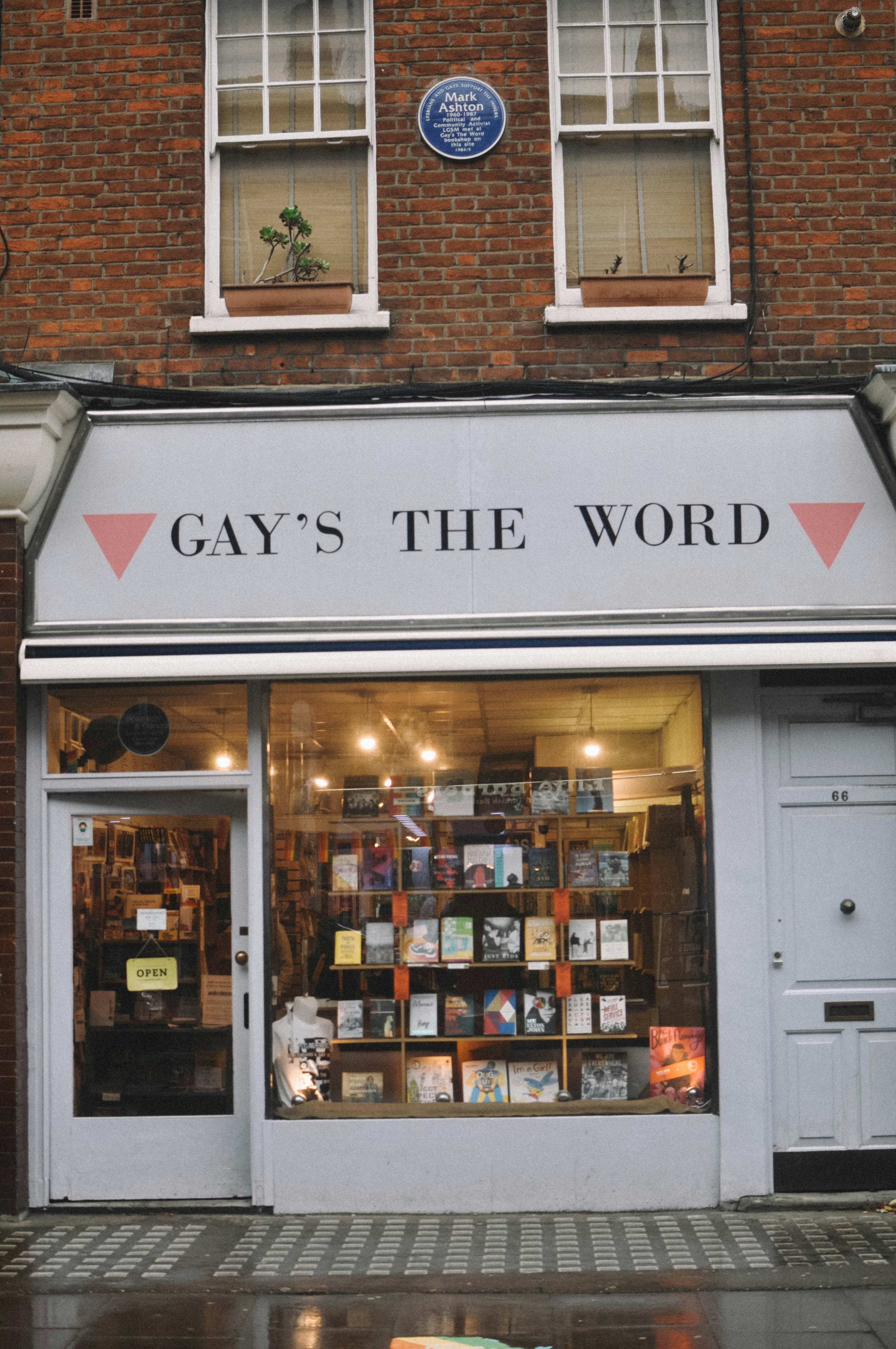 The white facade of Gay's the Word has pink triangles at the side of name. Books fill the window display, facing outwards.