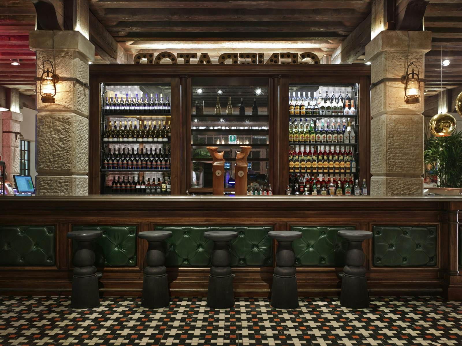 Bar of a hostel with green capped bar stools, wood paneling and dim lighting