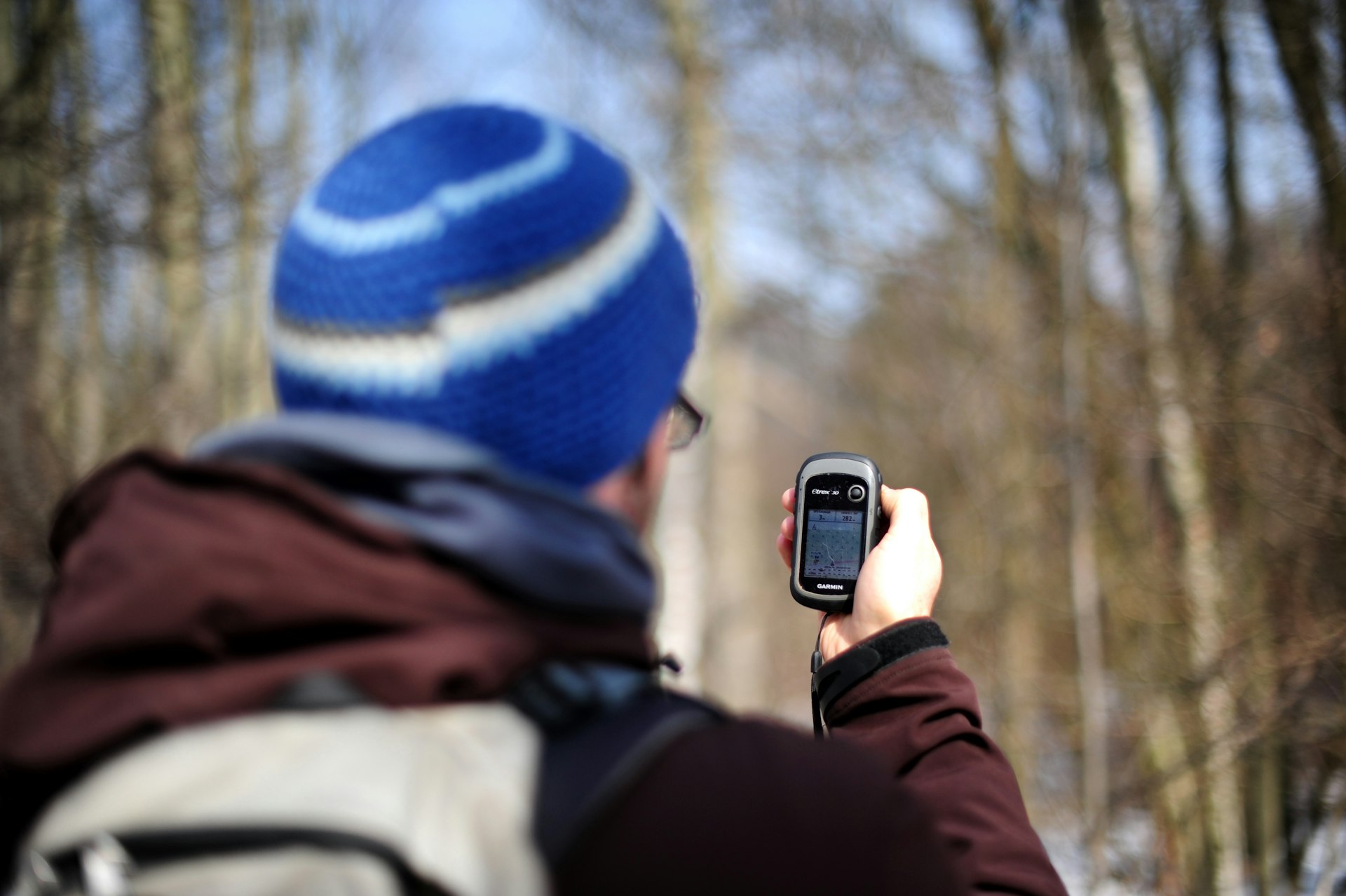 A man in a hat is geocaching, holding up his phone