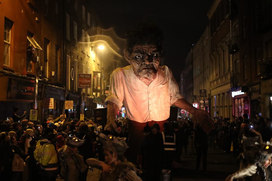 A giant monstrous effigy is paraded through the streets of Dublin as part of the Bram Stoker Festival. Around it, a large crowd watches on.