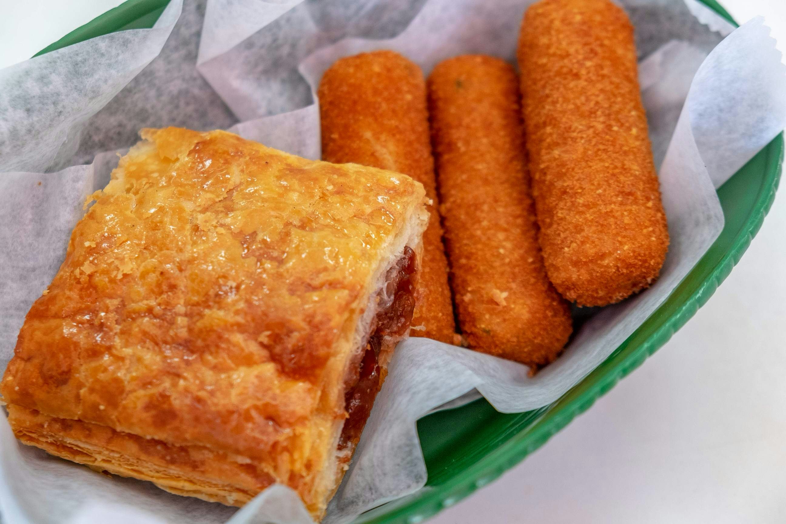 A green bowl is lined with white paper and three croquetas and a pastry are stacked inside.