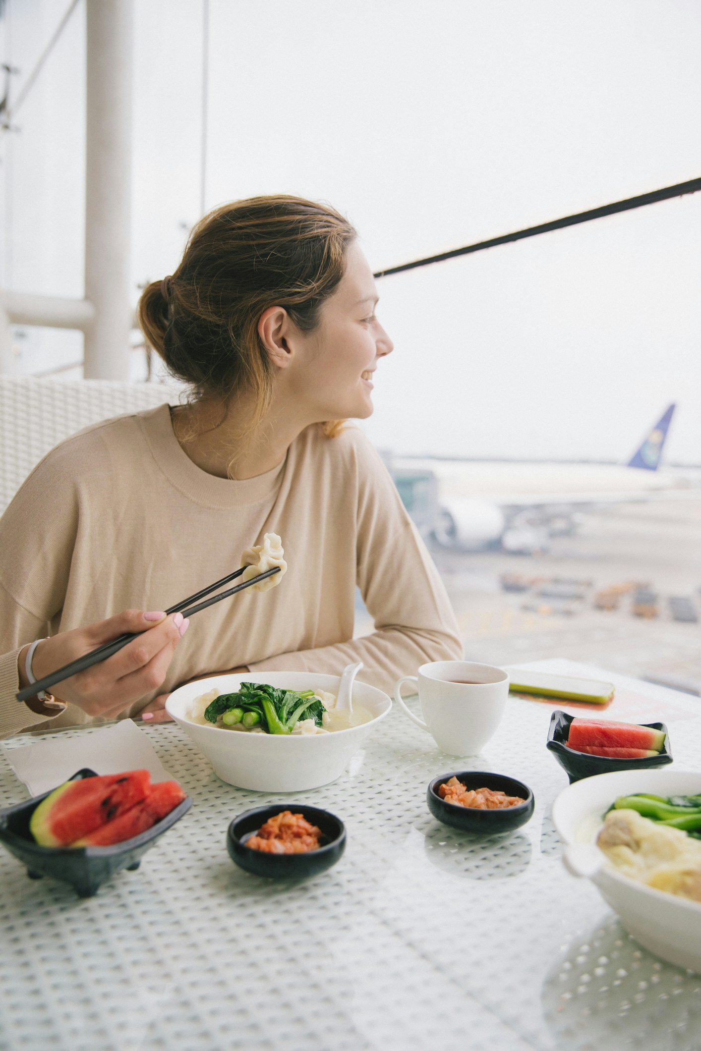 Woman Having Food In Restaurant While Looking Through Window At Airport