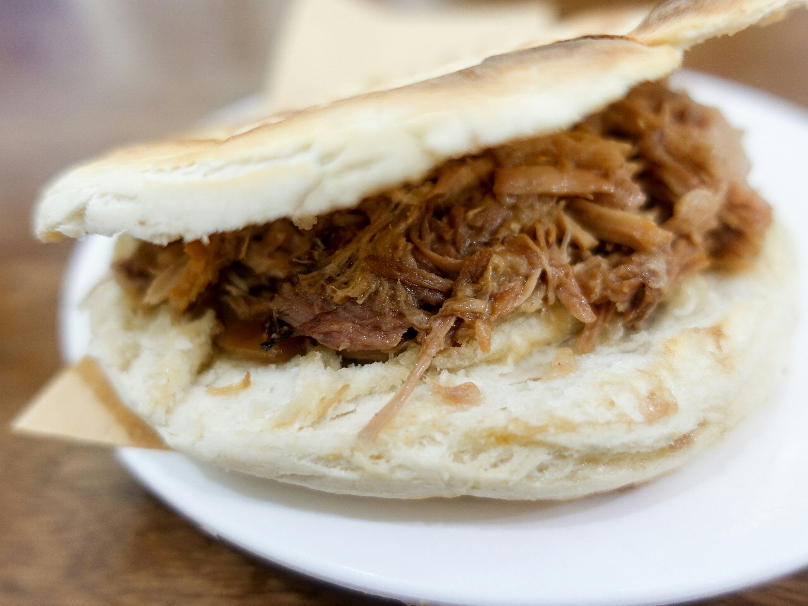 Juicy shredded beef is stuffed into an open bap. The sandwich is sitting on a white plate. 
