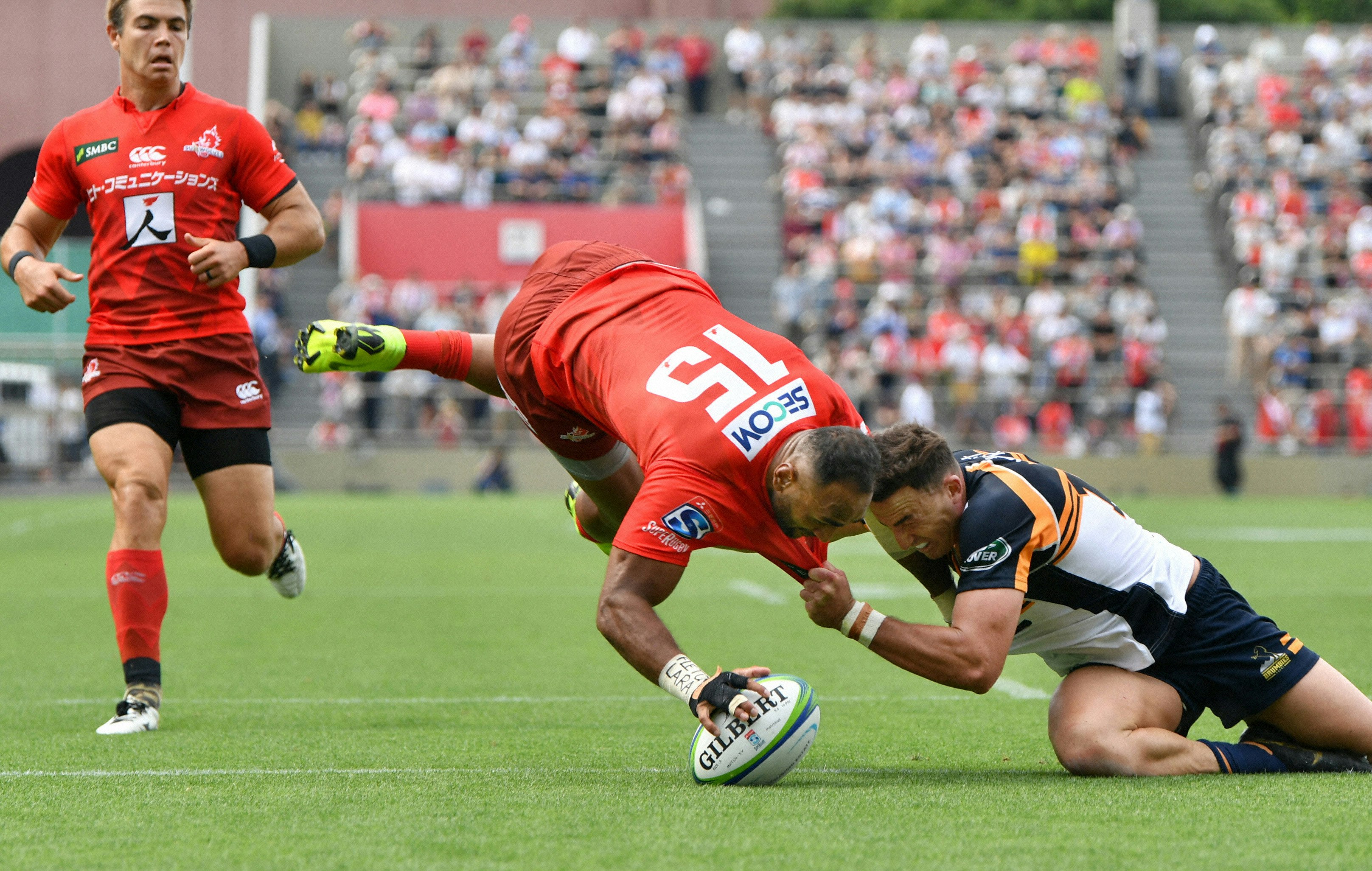 Semisi Masirewa of the Sunwolves scores a try during the Super Rugby match between Sunwolves and Brumbies at the Prince Chichibu Memorial Ground. The player is touching the ball on the ground while leaping into the air, with his legs above his head.
