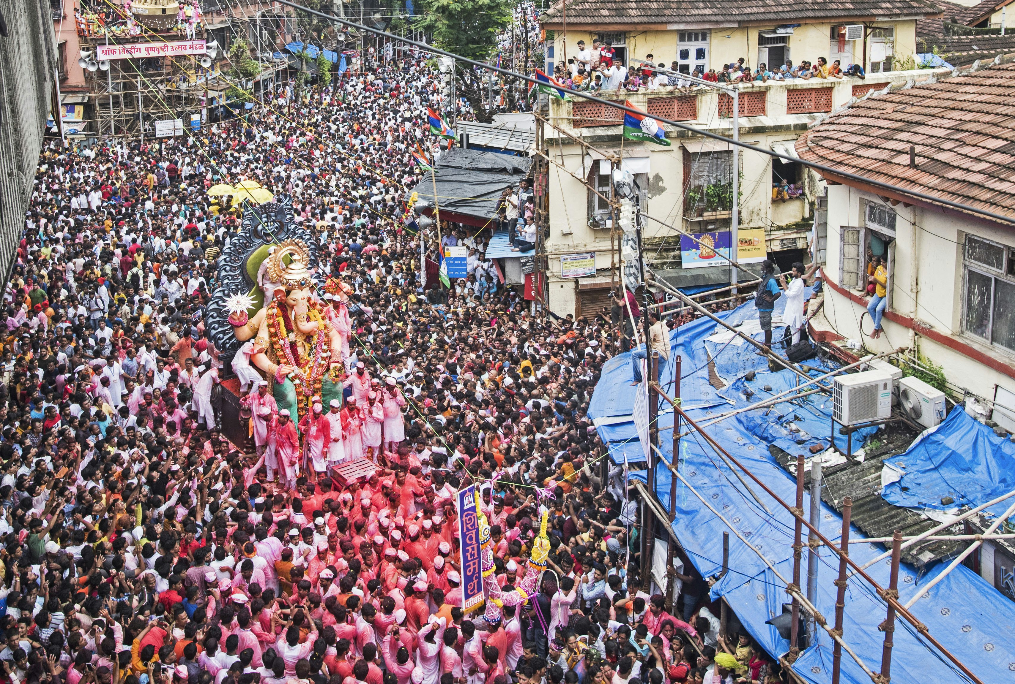 A mammoth crowd floods the streets of Mumbai, surrounding an effigy of Hindu god Ganesh. People also watch on from windows and rooftops.