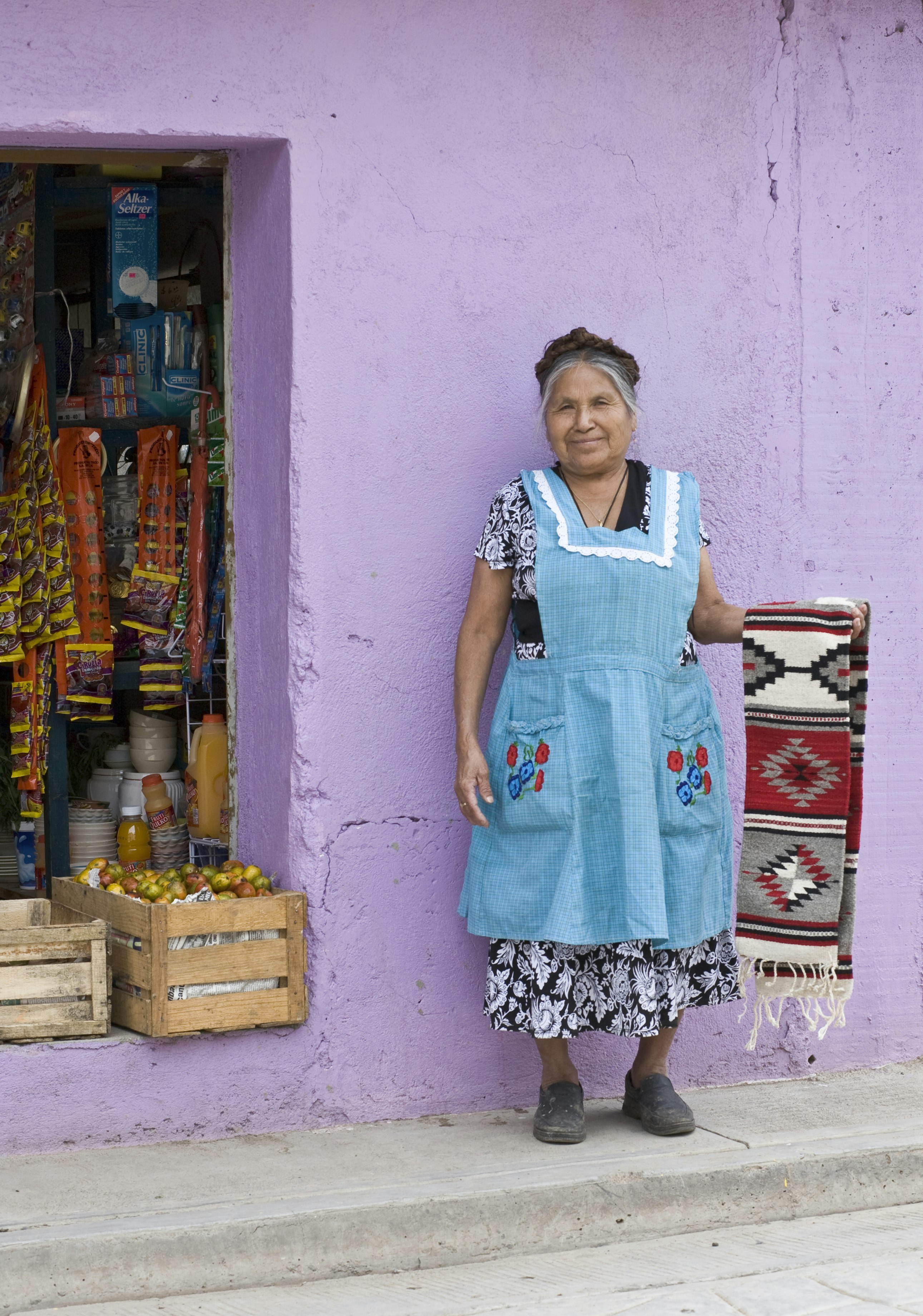 Friendly, smiling local indigenous Mexican woman vendor displaying handwoven Zapotec rug outside shop