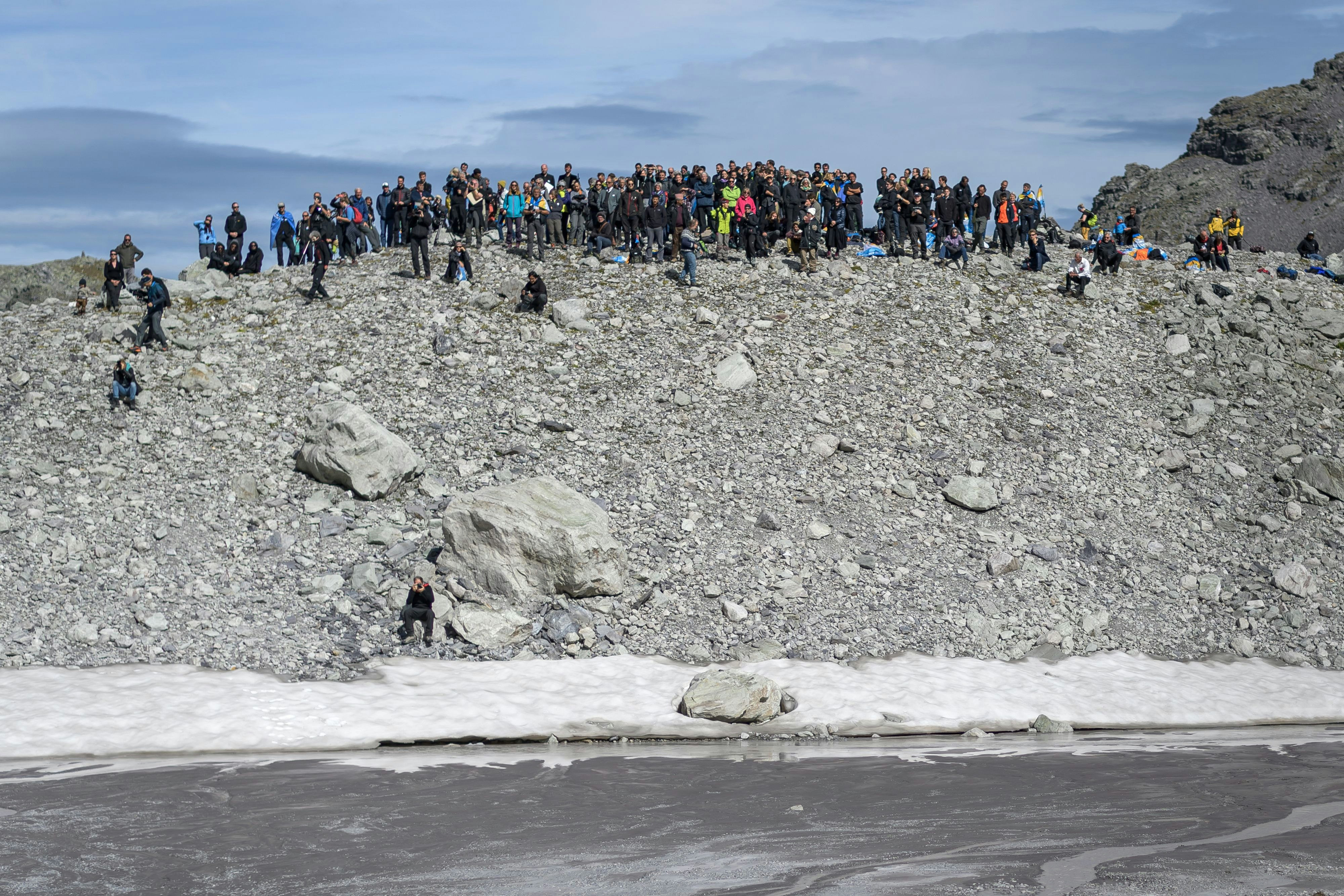 Hundreds of people dressed in black stand above the disappearing Pizol glacier