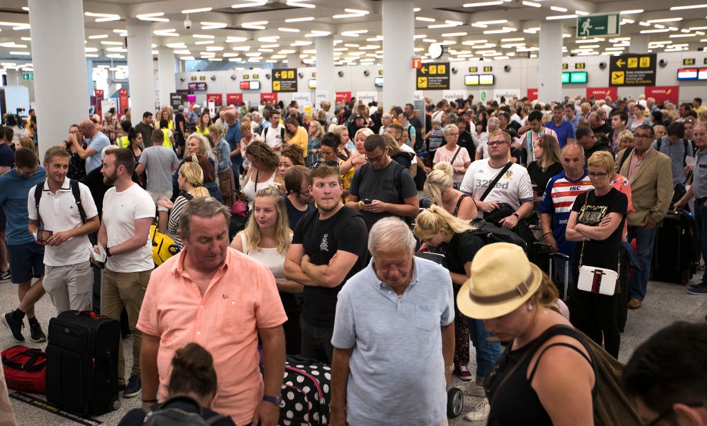 Crowds of people stand in an airport waiting. 